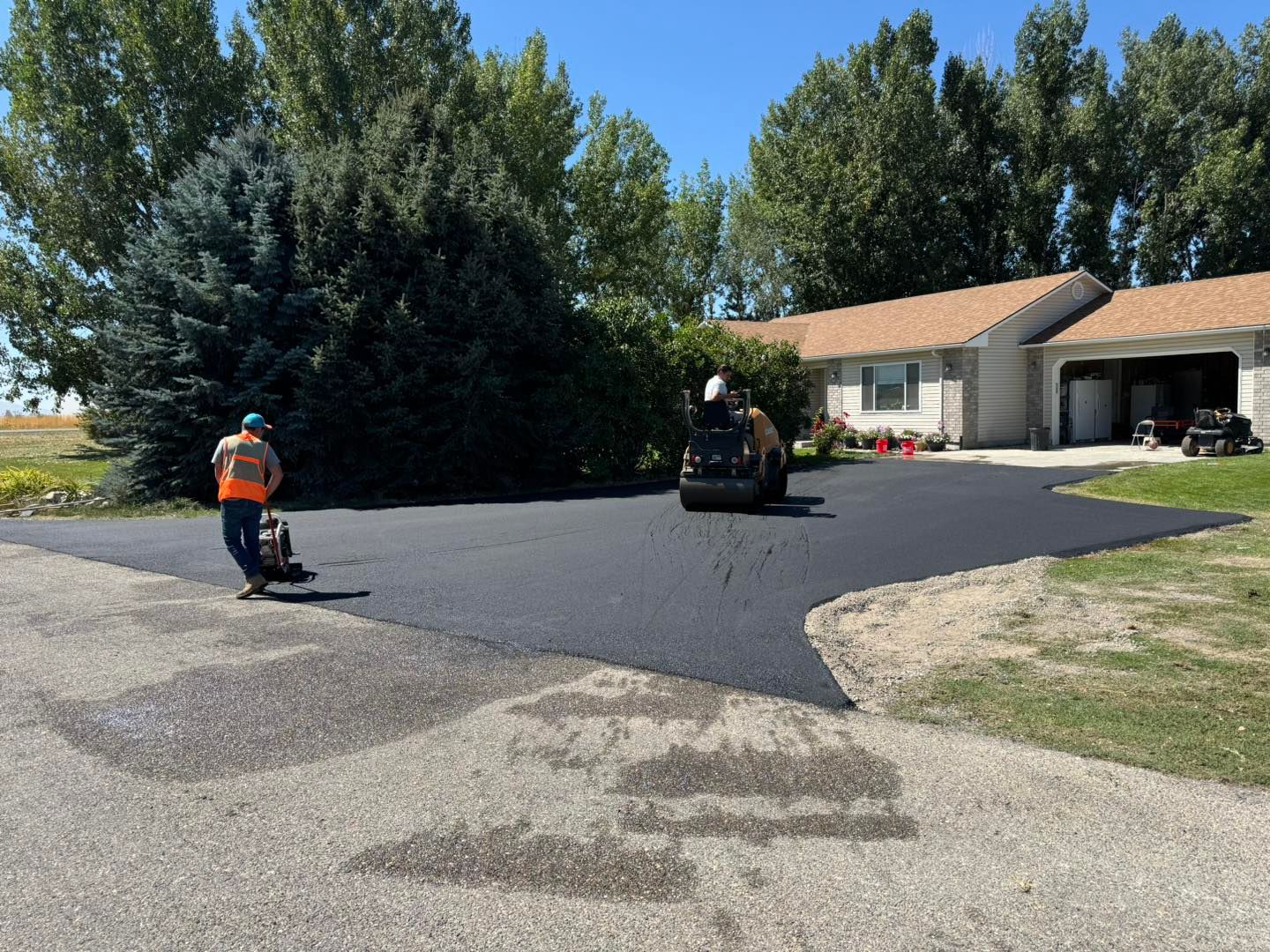 Asphalt paving a driveway in front of a house; workers operate machinery.