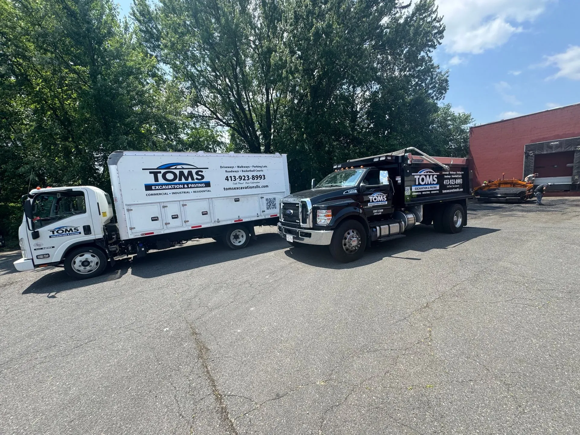 Two service trucks, one white and one black, parked outside. Trees in background.