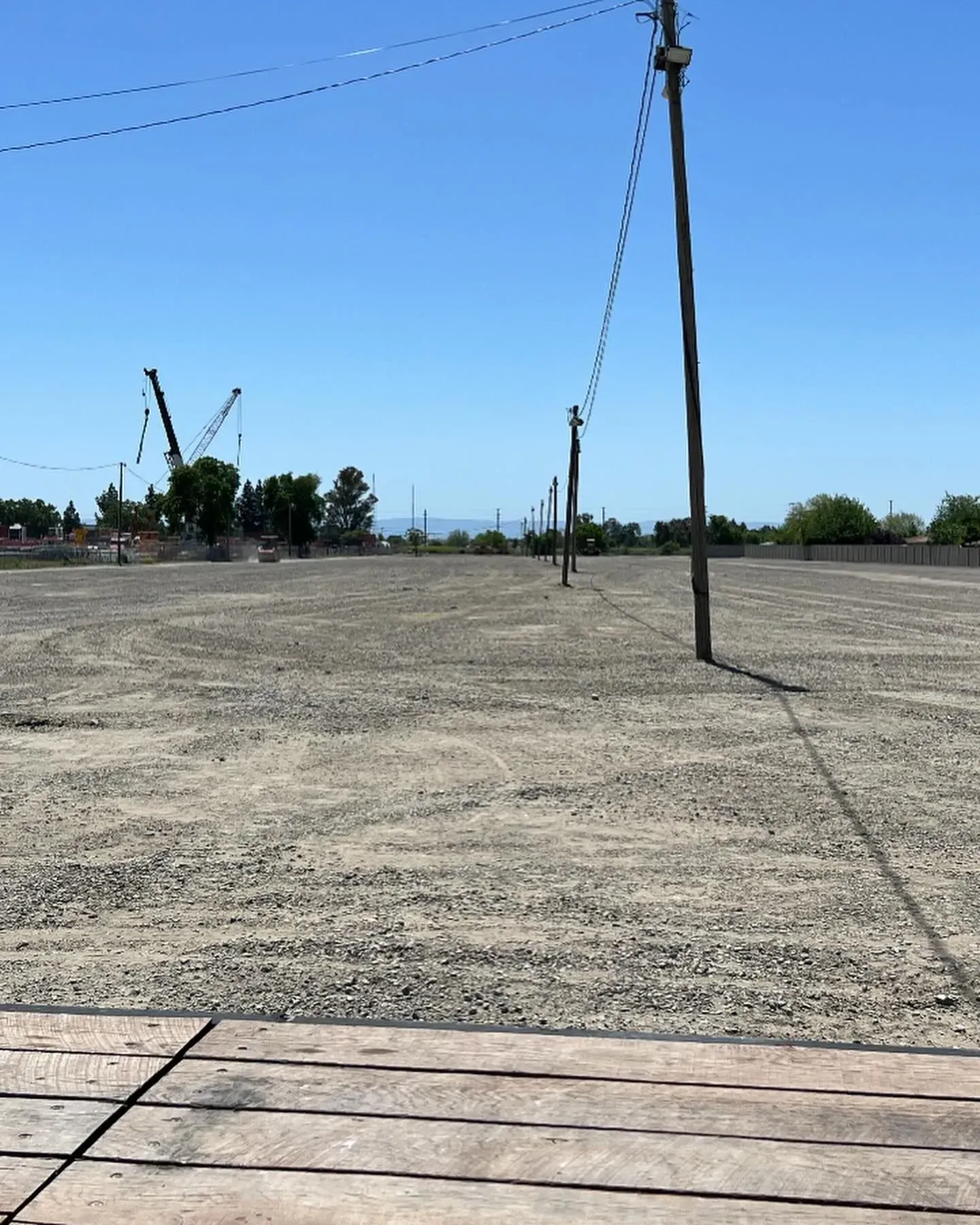 A flat, gravel lot with power lines overhead and construction cranes visible in the distance.
