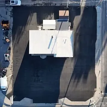 Overhead view of a commercial building with a large asphalt parking lot. Cars and a truck are parked nearby.