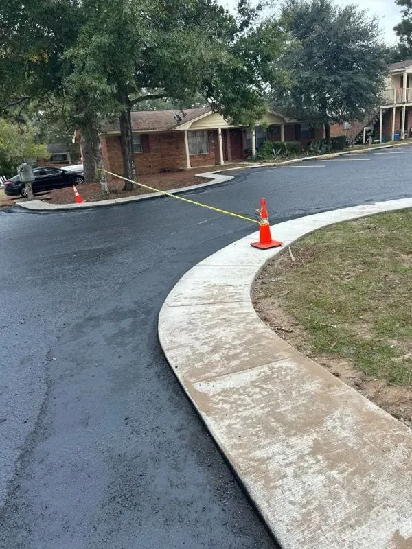 Freshly paved asphalt street with sidewalk, caution tape, and traffic cones.