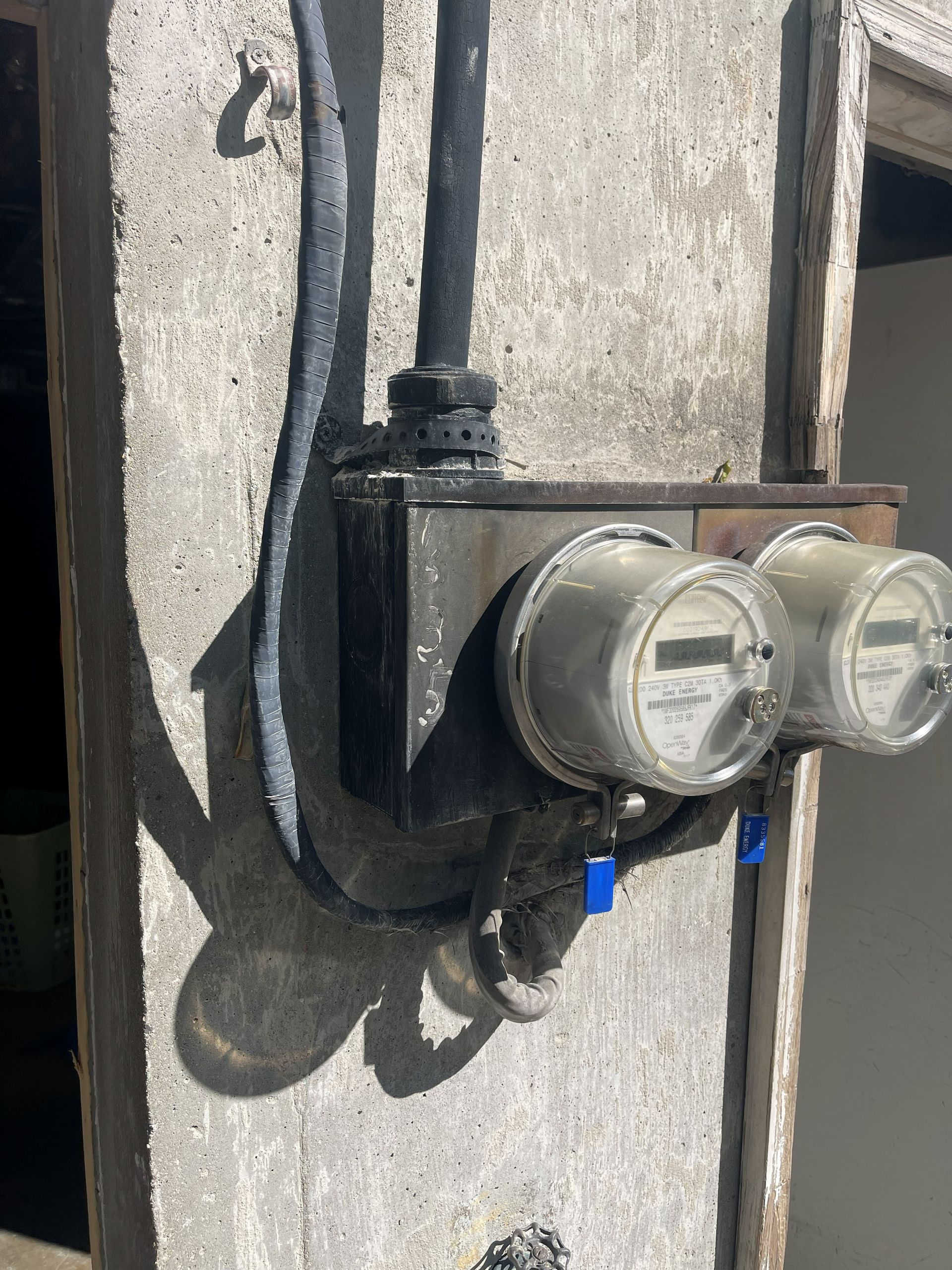 Two electric meters on a concrete pillar with black wires and a metal box.