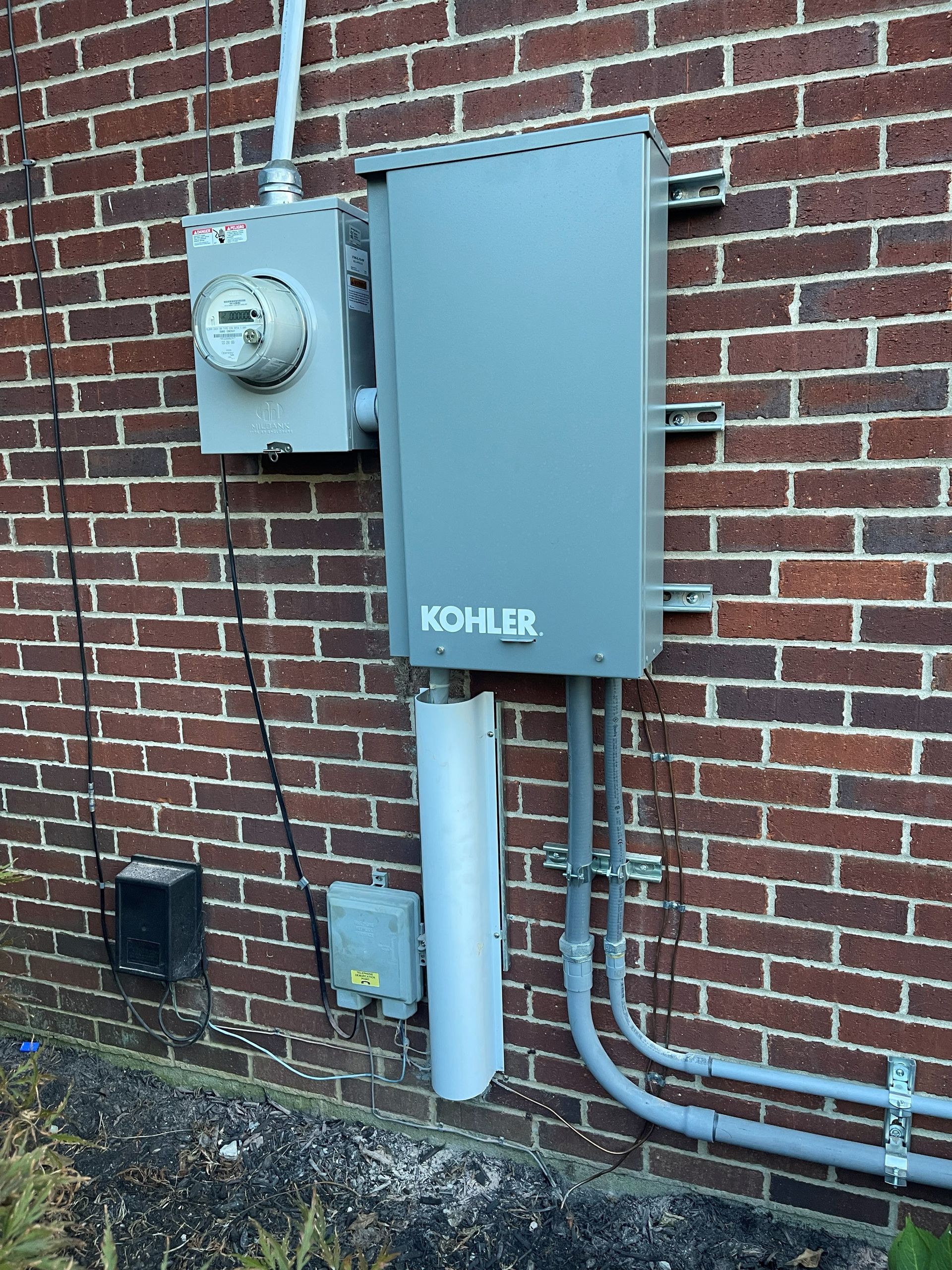 Electrical components mounted on a brick wall, including a Kohler generator box and meter.