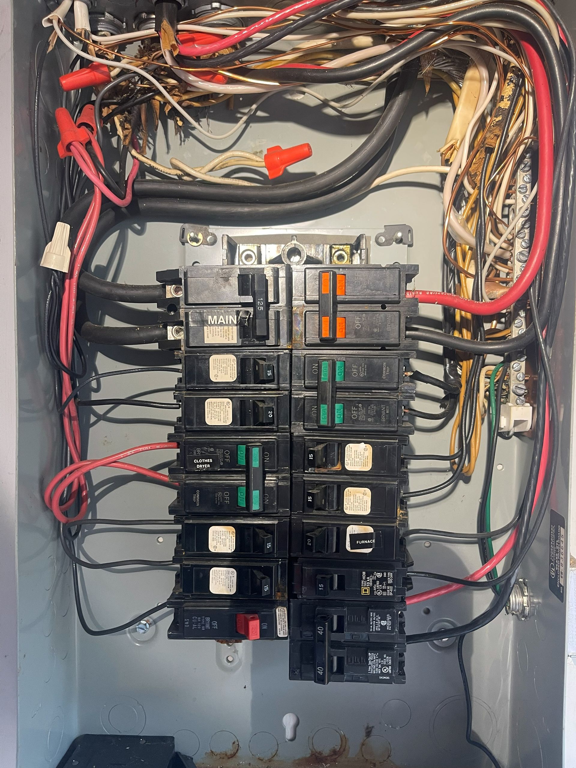 Electrical panel with black and red wires, circuit breakers, and exposed wiring.