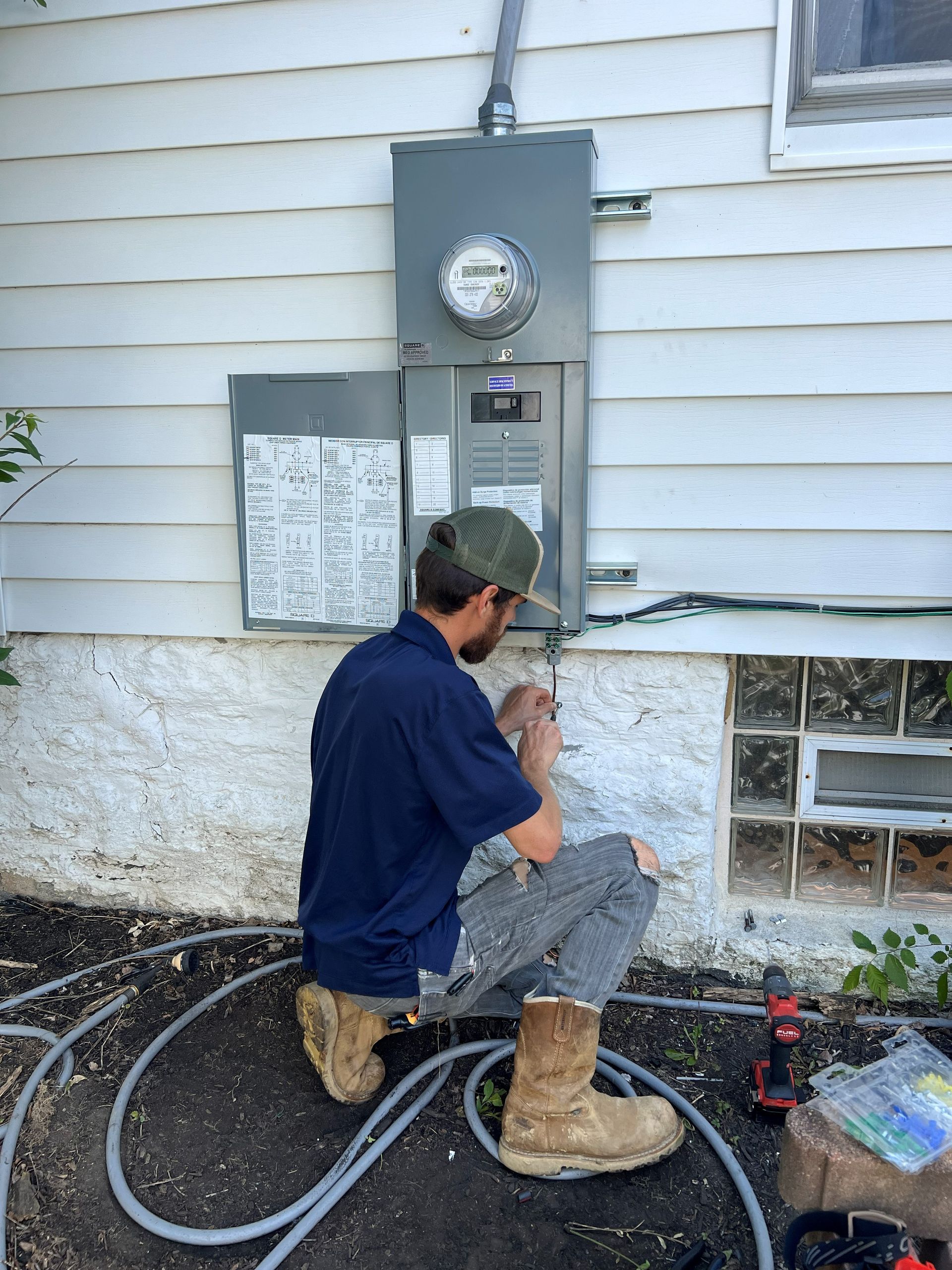 Man crouches, working on electrical box on the side of a house.