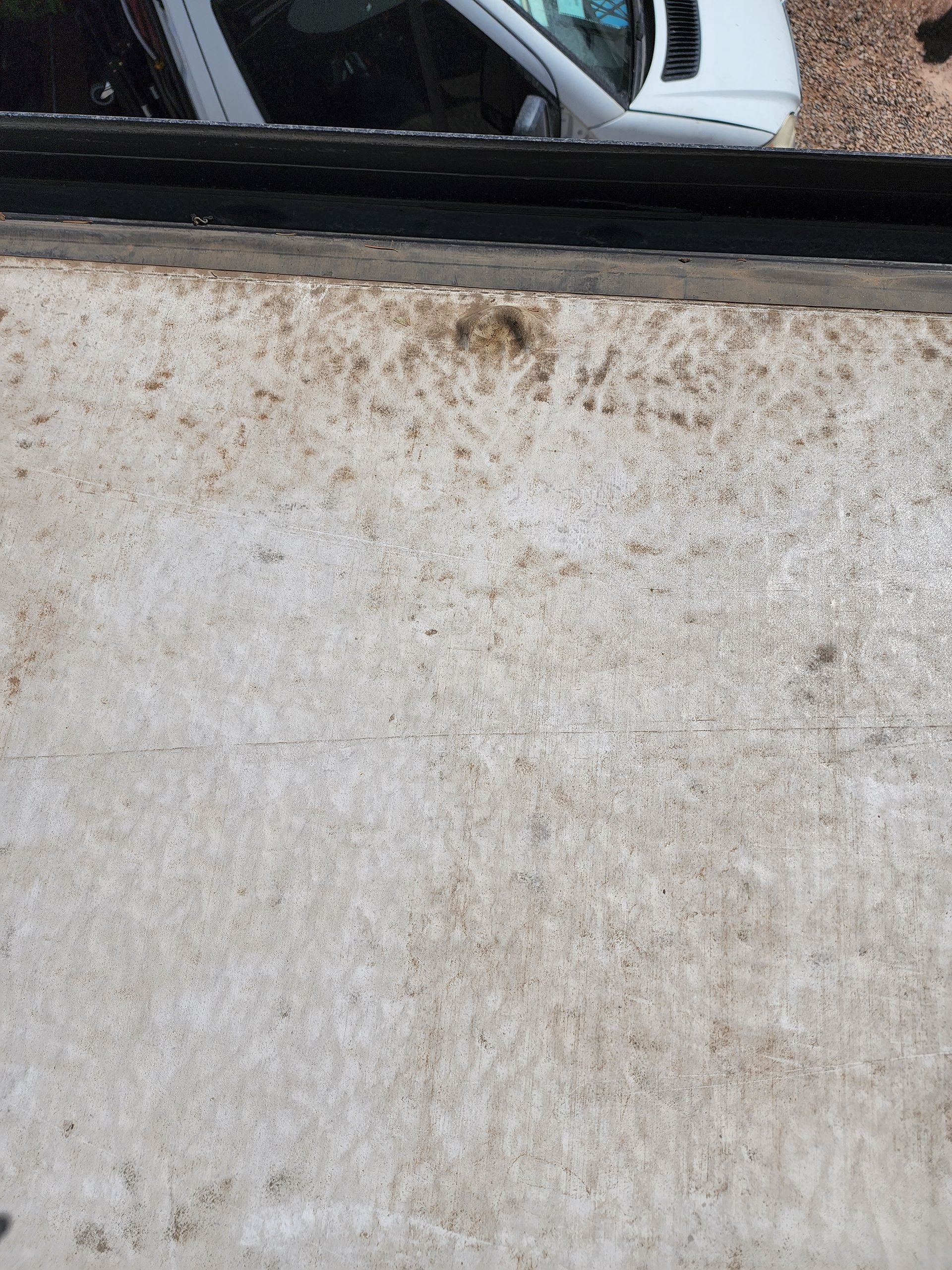 Dirty white surface with dark smudges, part of a white vehicle in the background.