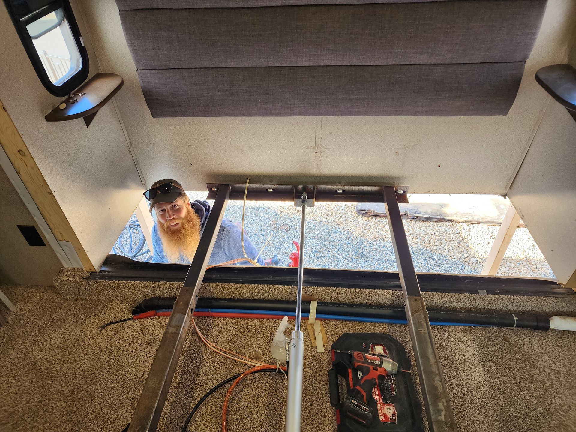 Person looking up into a RV frame, appears to be working on electrical or plumbing with tools visible.