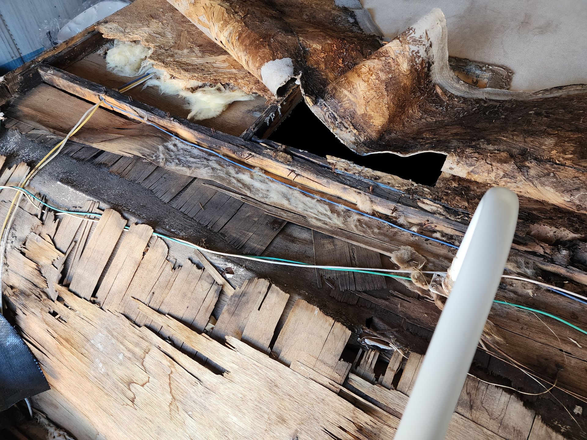 Damaged roof showing rotten wood, exposed insulation, and a hole.