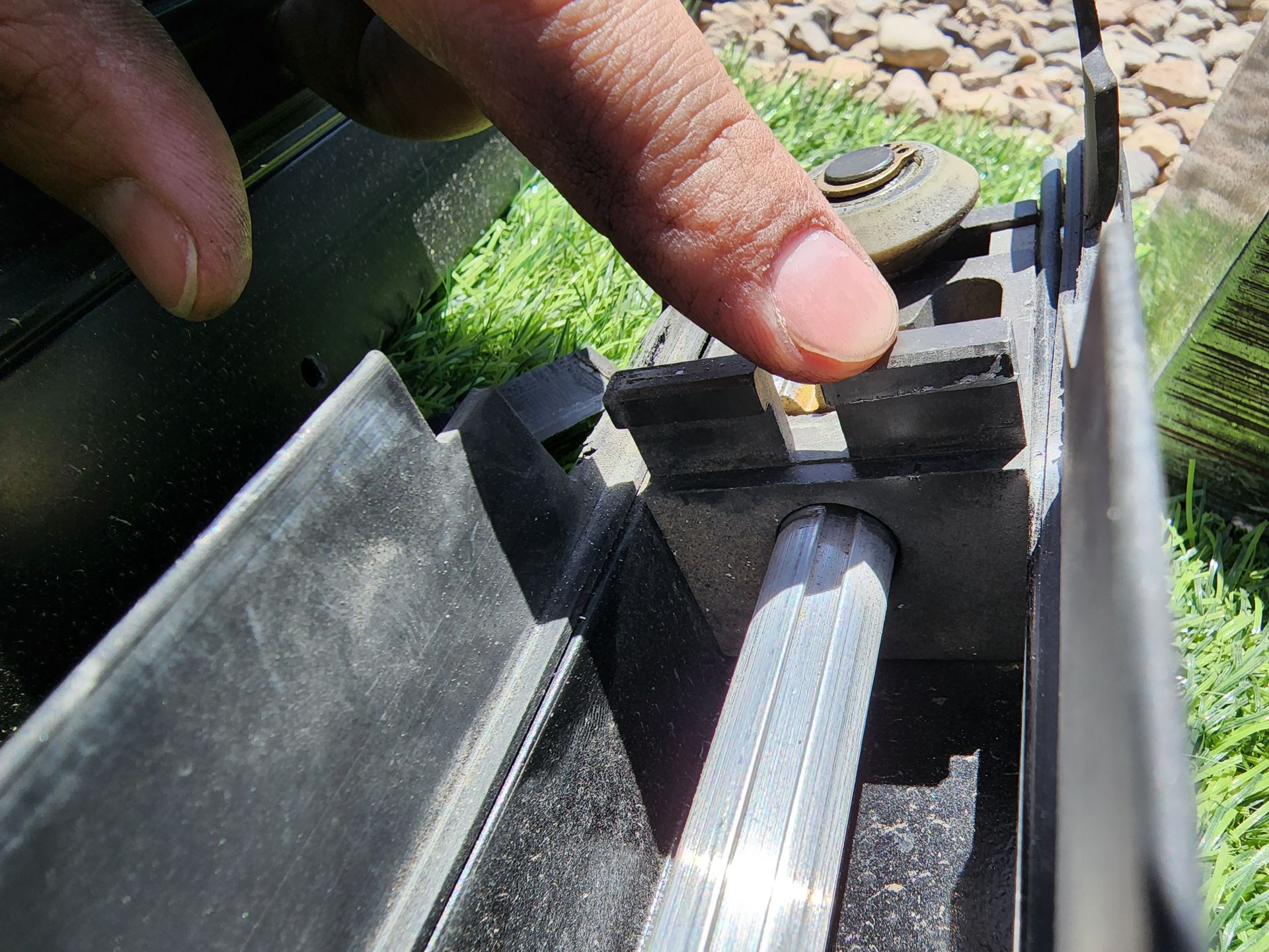 Finger pointing at a small metal piece within a black, rectangular frame. Silver bar visible below.