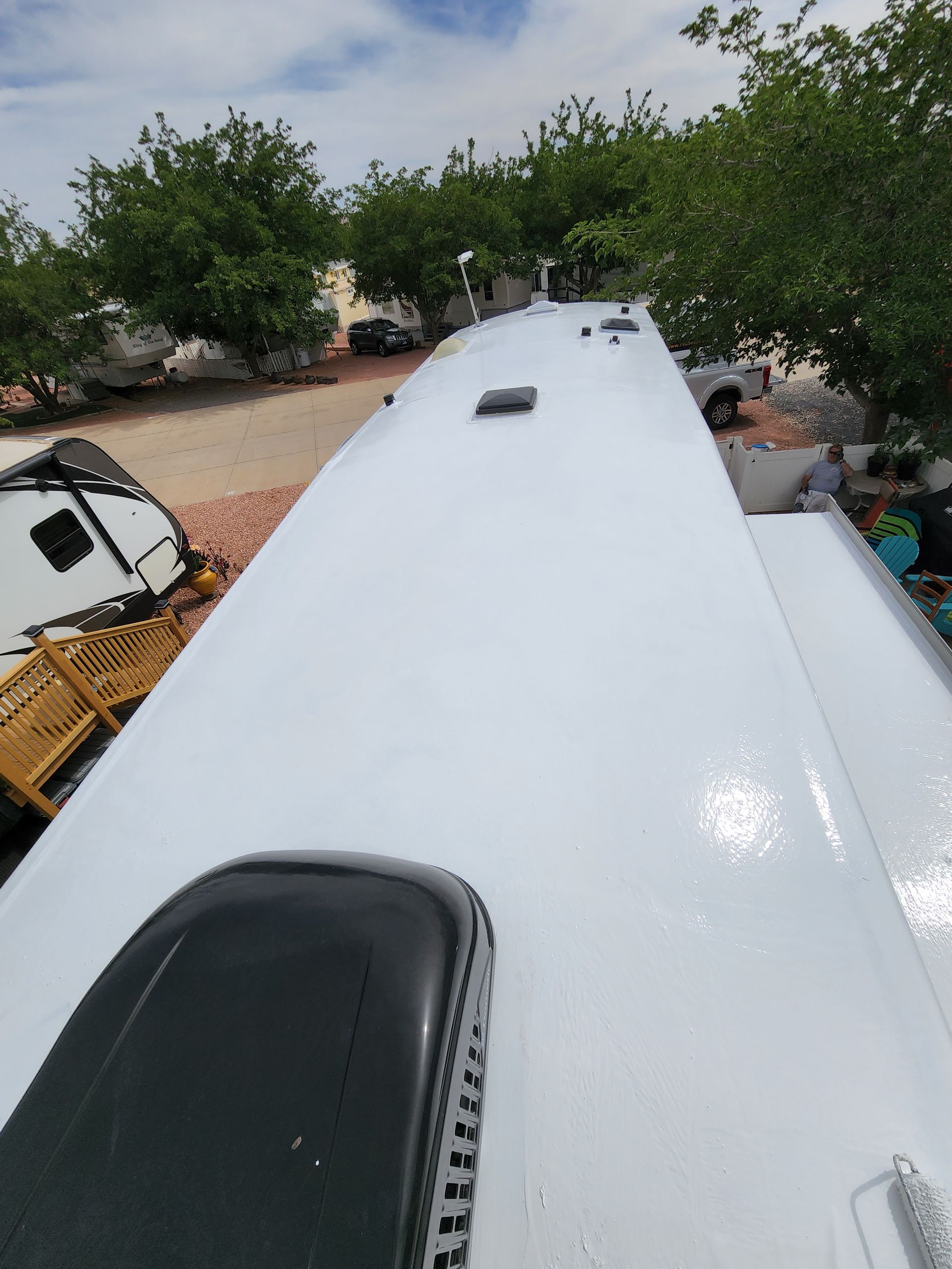 White RV roof with air conditioning unit, vents, and surrounding trees.