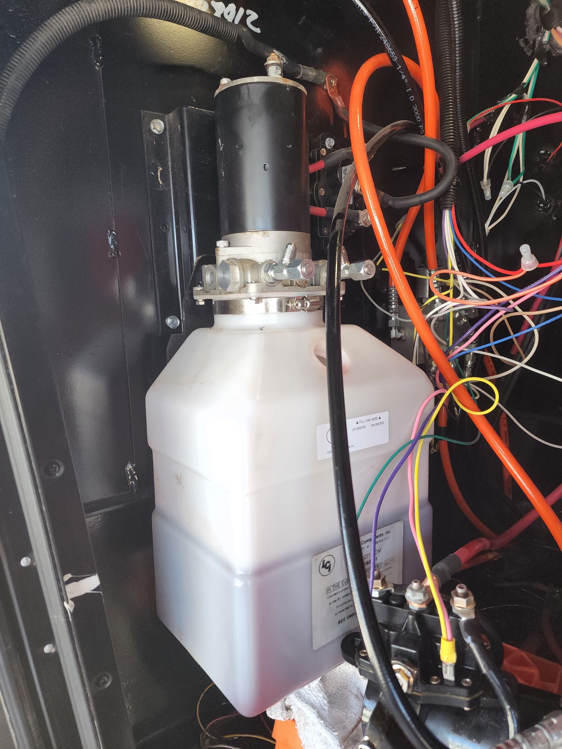 Hydraulic leveling system components mounted in a compartment, with wiring and orange tubing.