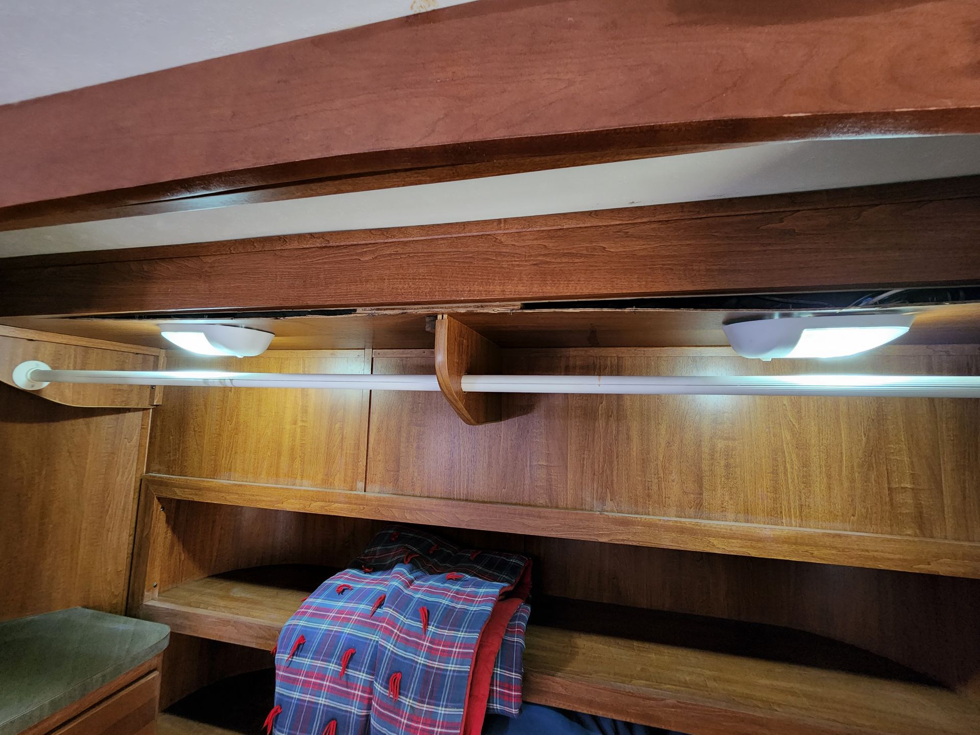 Interior of a wooden boat with a shelf, clothes rack, and two overhead lights.