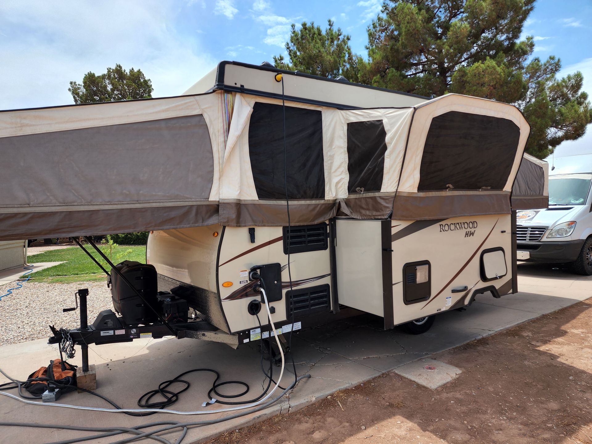 Beige and brown pop-up camper with extended canvas sections, parked outside.