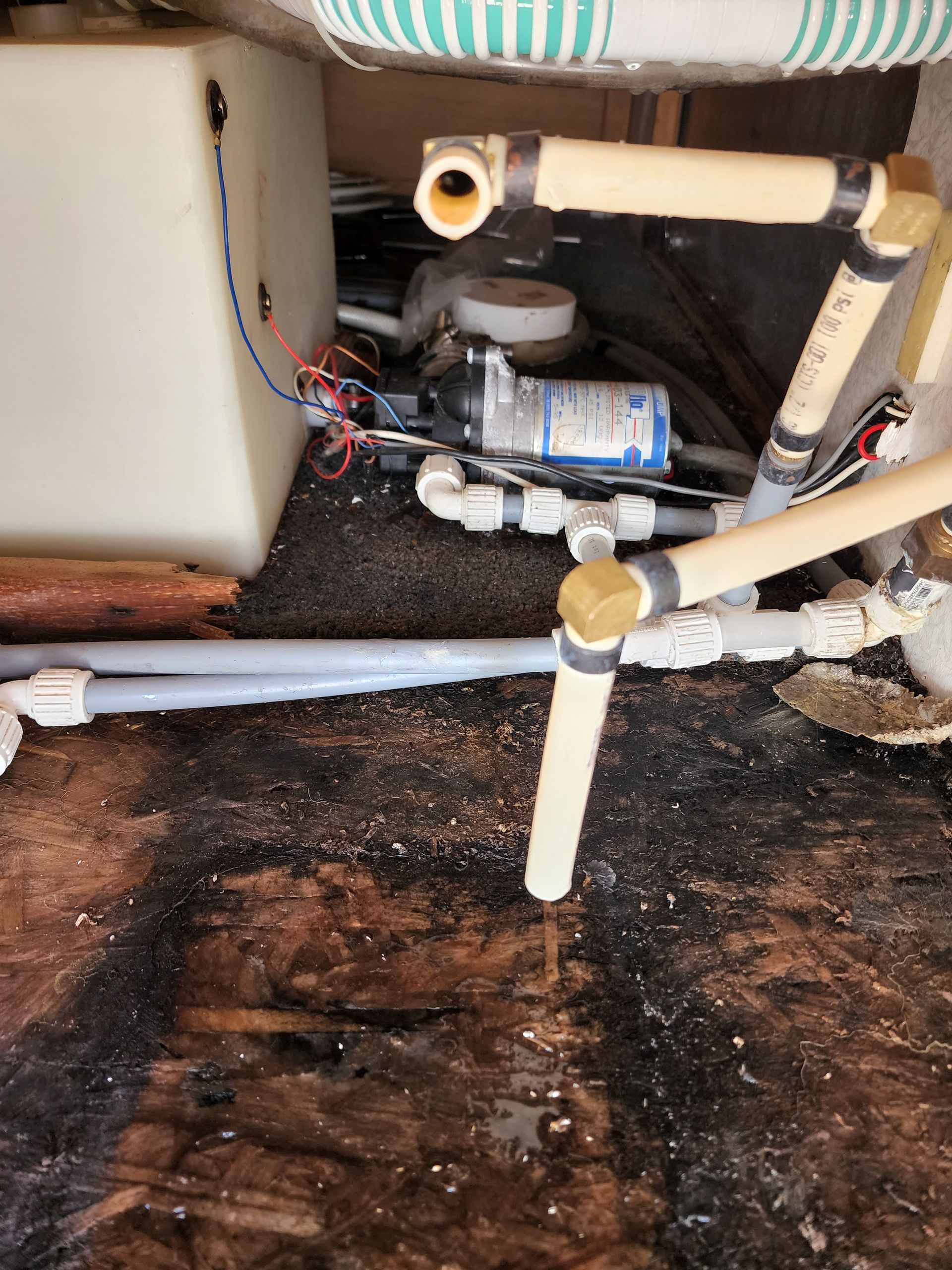 RV plumbing system with water pump, piping, and tank. Damaged floor.