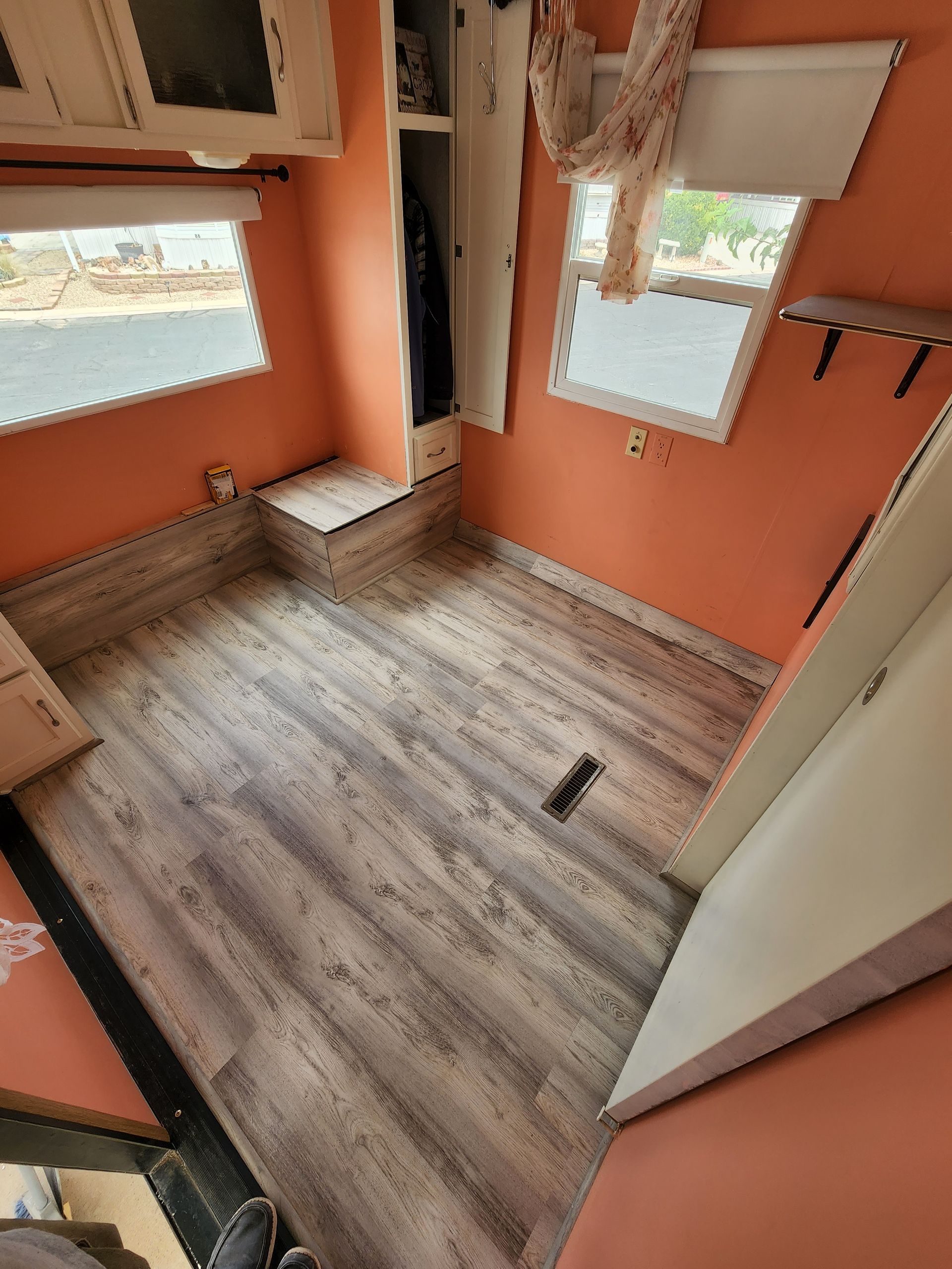 Interior of a small room with orange walls, wood-look flooring, two windows, and a closet.