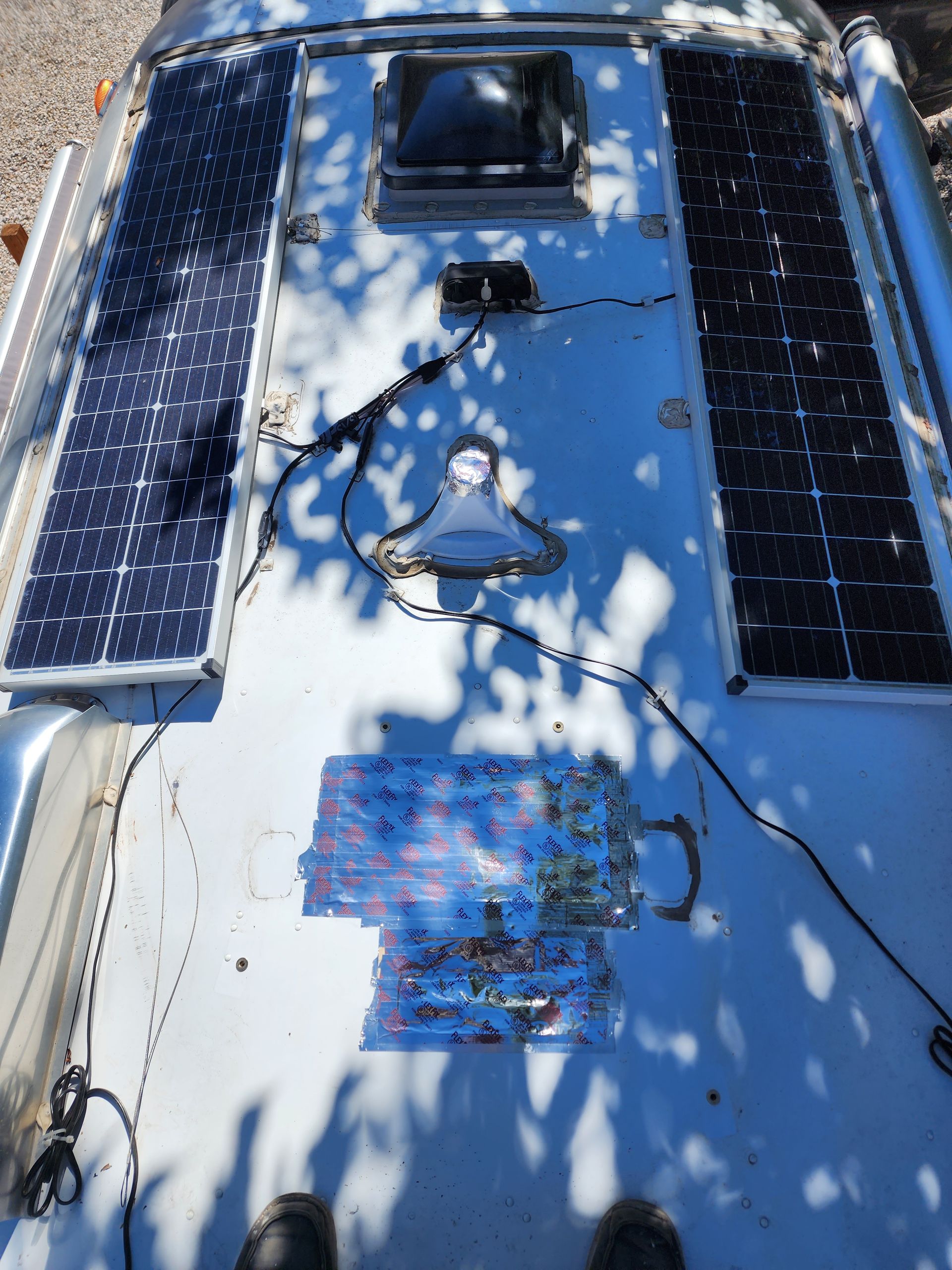 Solar panels on the roof of a camper van with various wires and a vent.