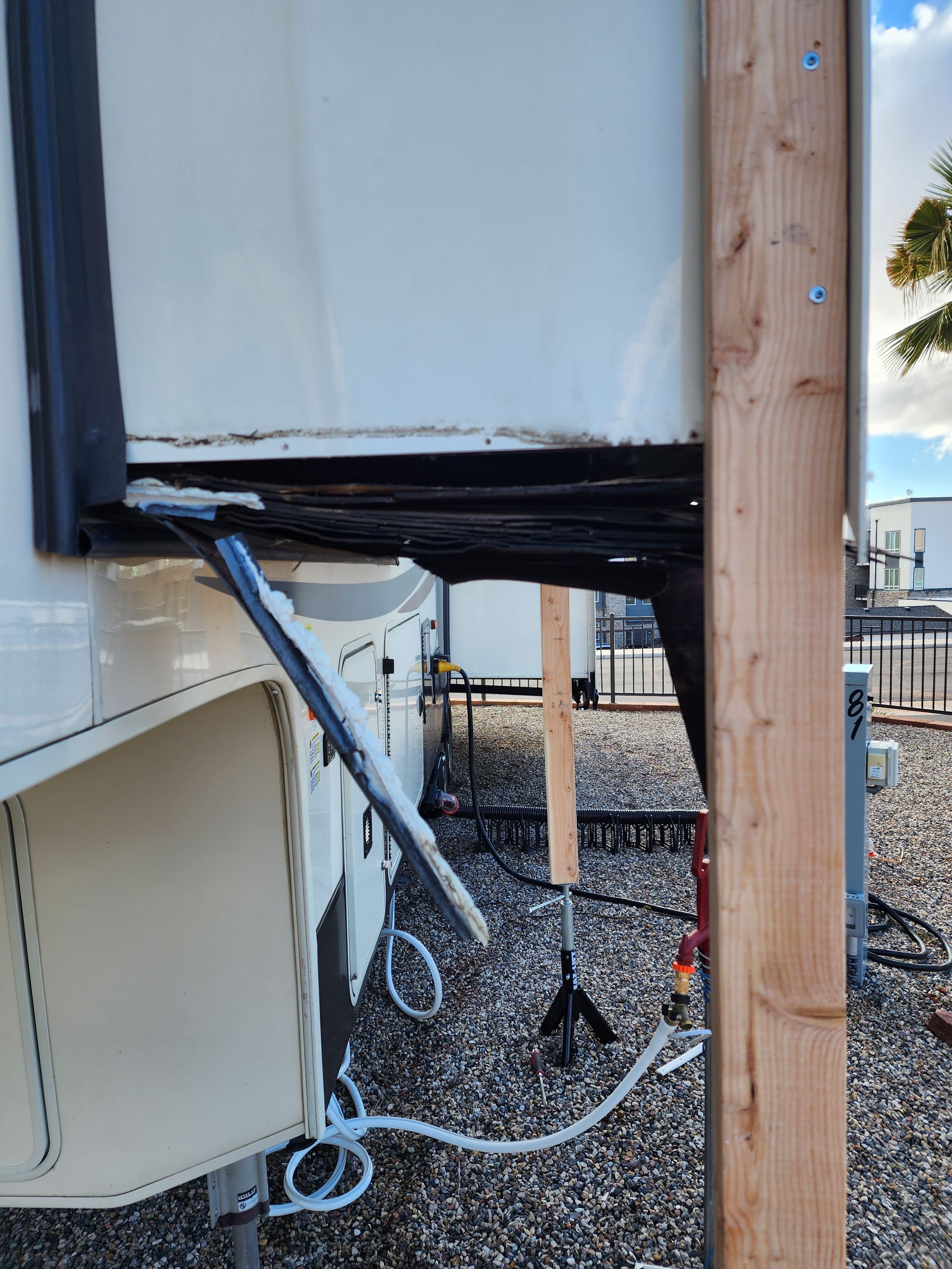 RV damage: Ripped awning and torn seal near a wooden support post. Exterior shot.