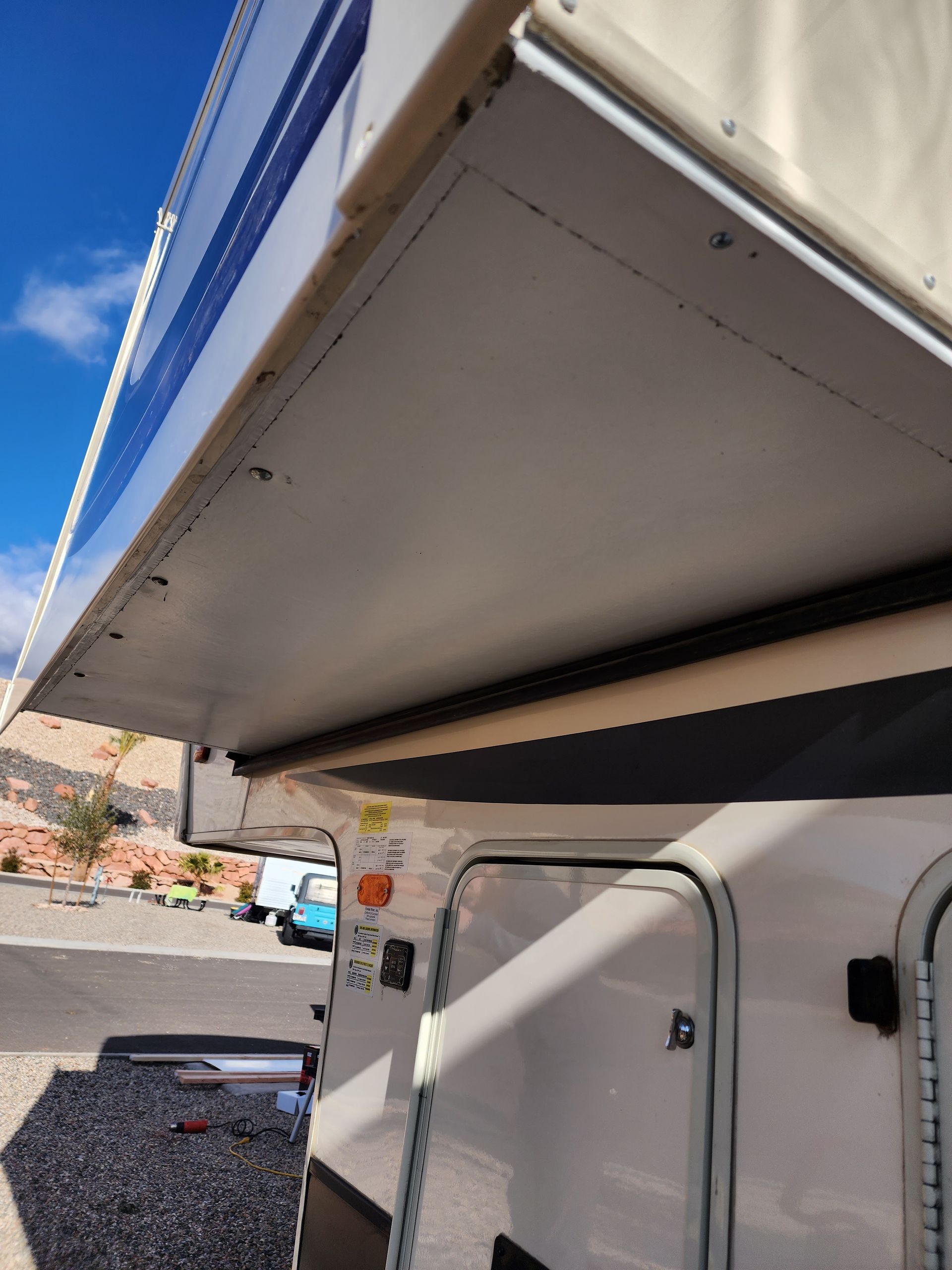White RV camper with a partially extended awning, blue sky in the background.