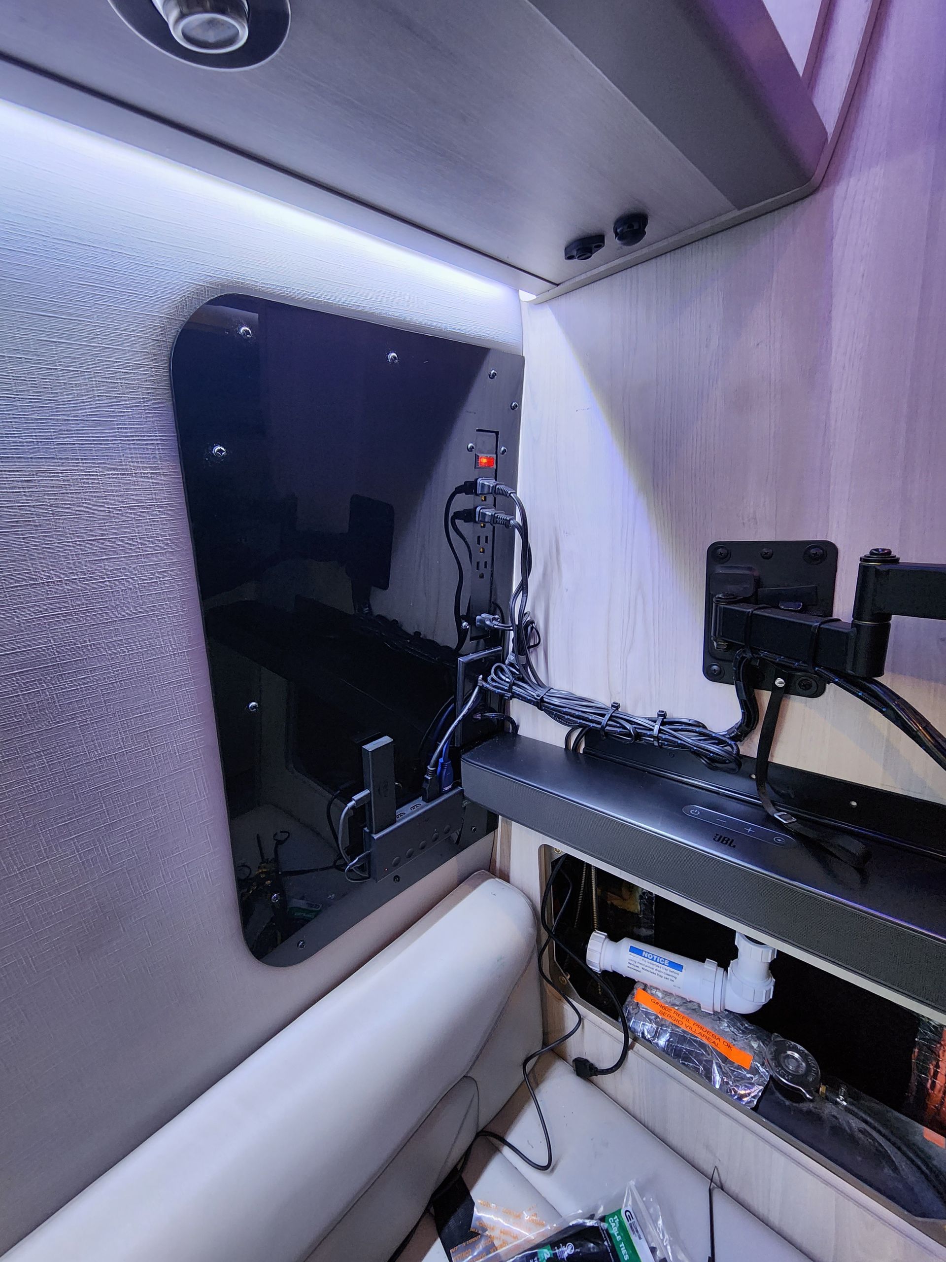 Interior of a vehicle, angled shot. Wall-mounted monitor, controls, and shelving, illuminated by overhead lighting.