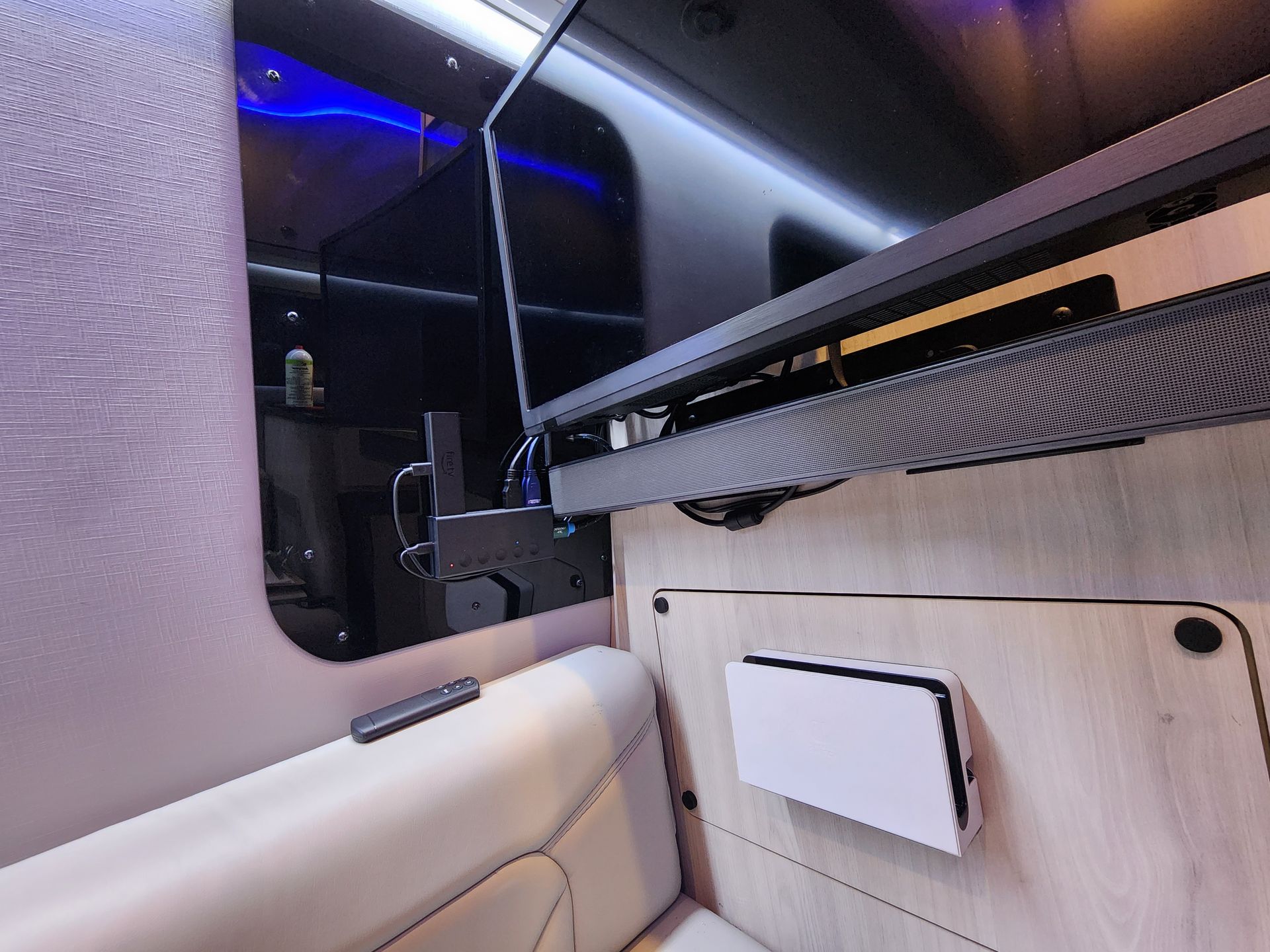 Inside a recreational vehicle, a television is mounted on a mechanical arm, extending from the wall. A soundbar and electronics are beneath.