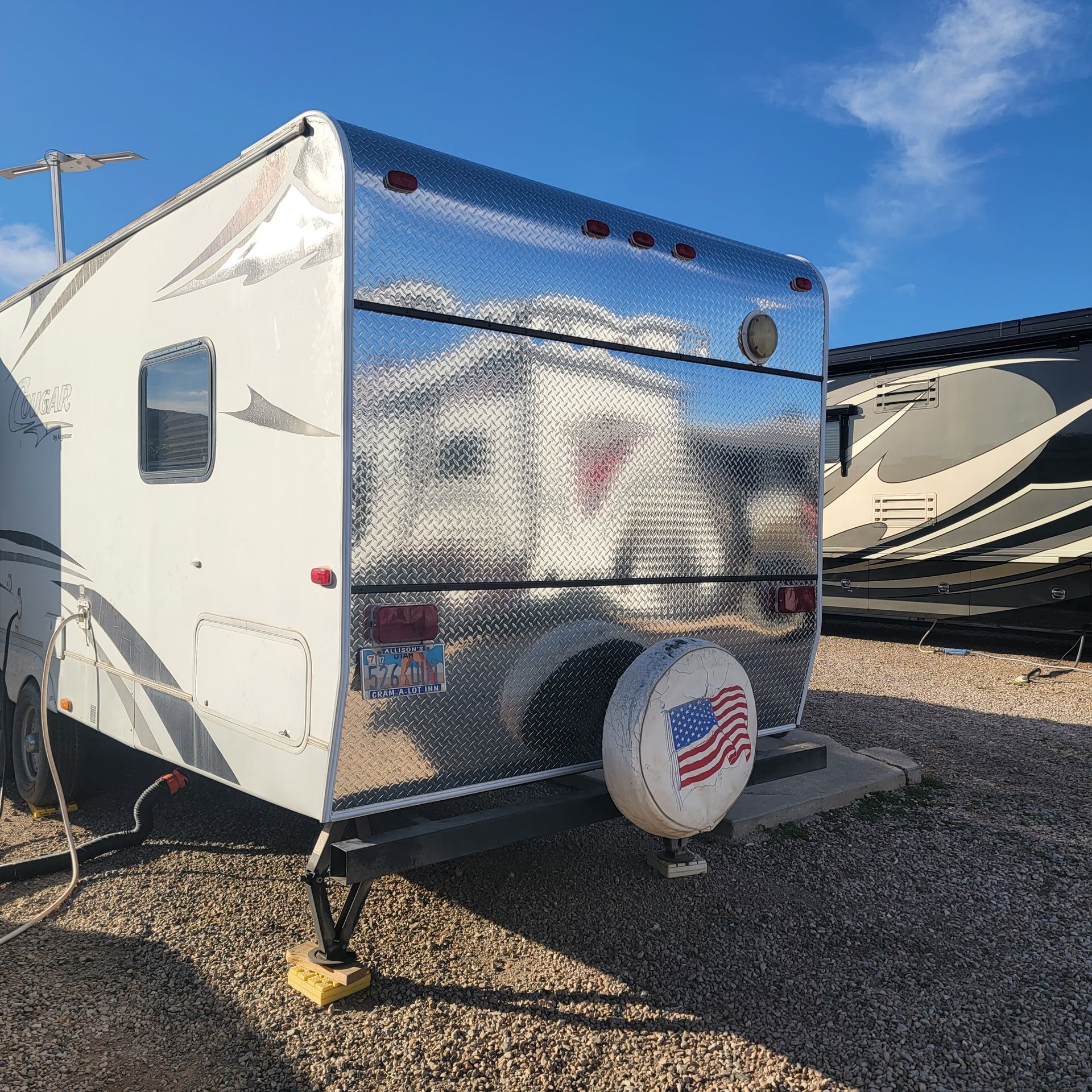 Travel trailer with reflective diamond plate paneling. A spare tire cover shows an American flag.