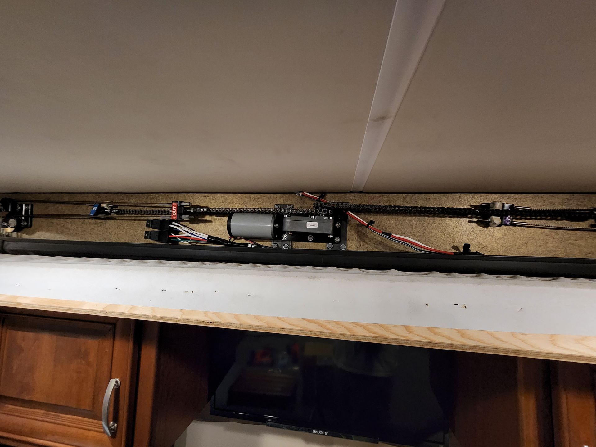 Motorized mechanism for a slide-out RV feature, mounted under ceiling, with wires and gears.