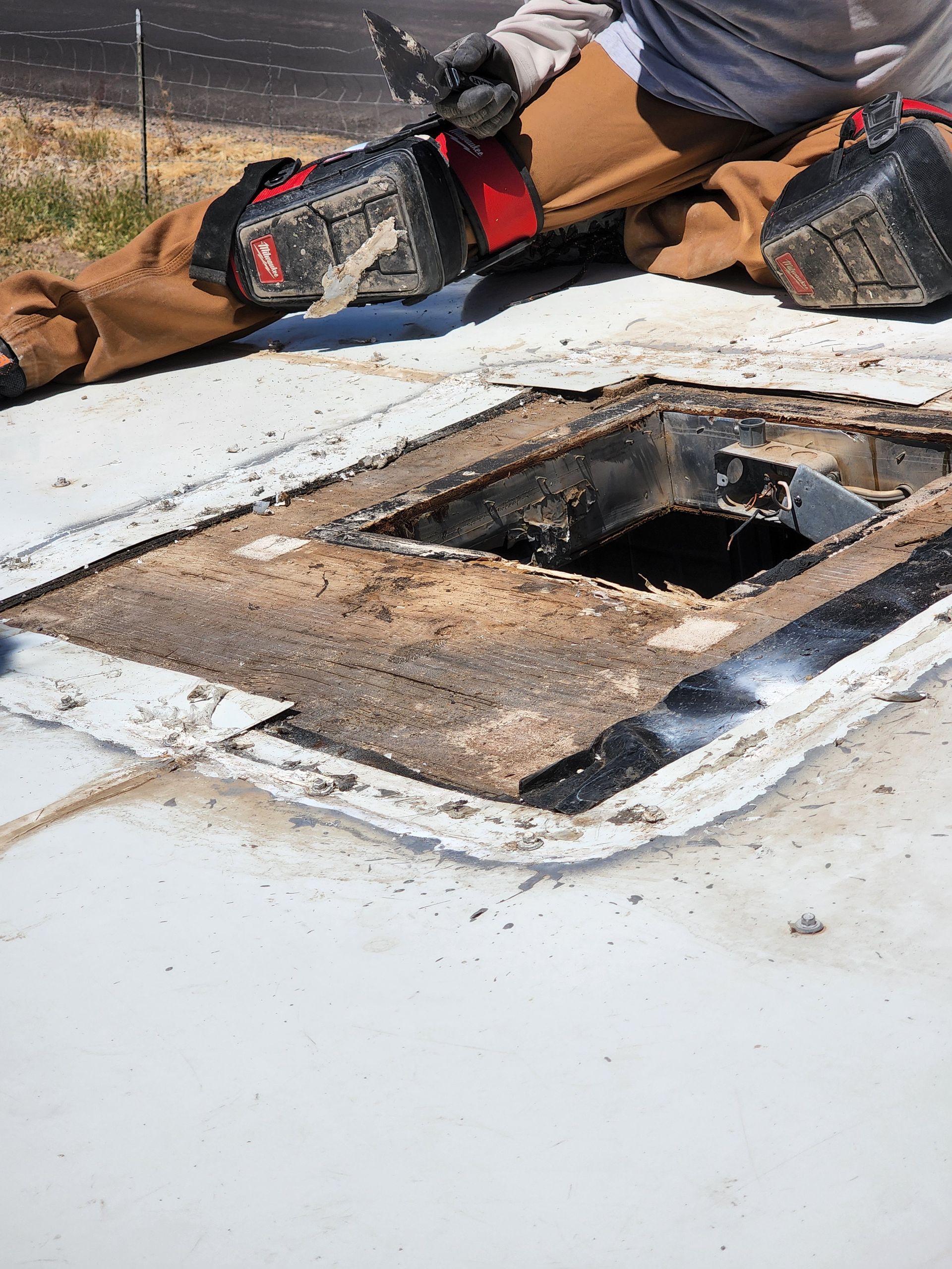 Person kneeling on white RV roof, working on a roof vent.