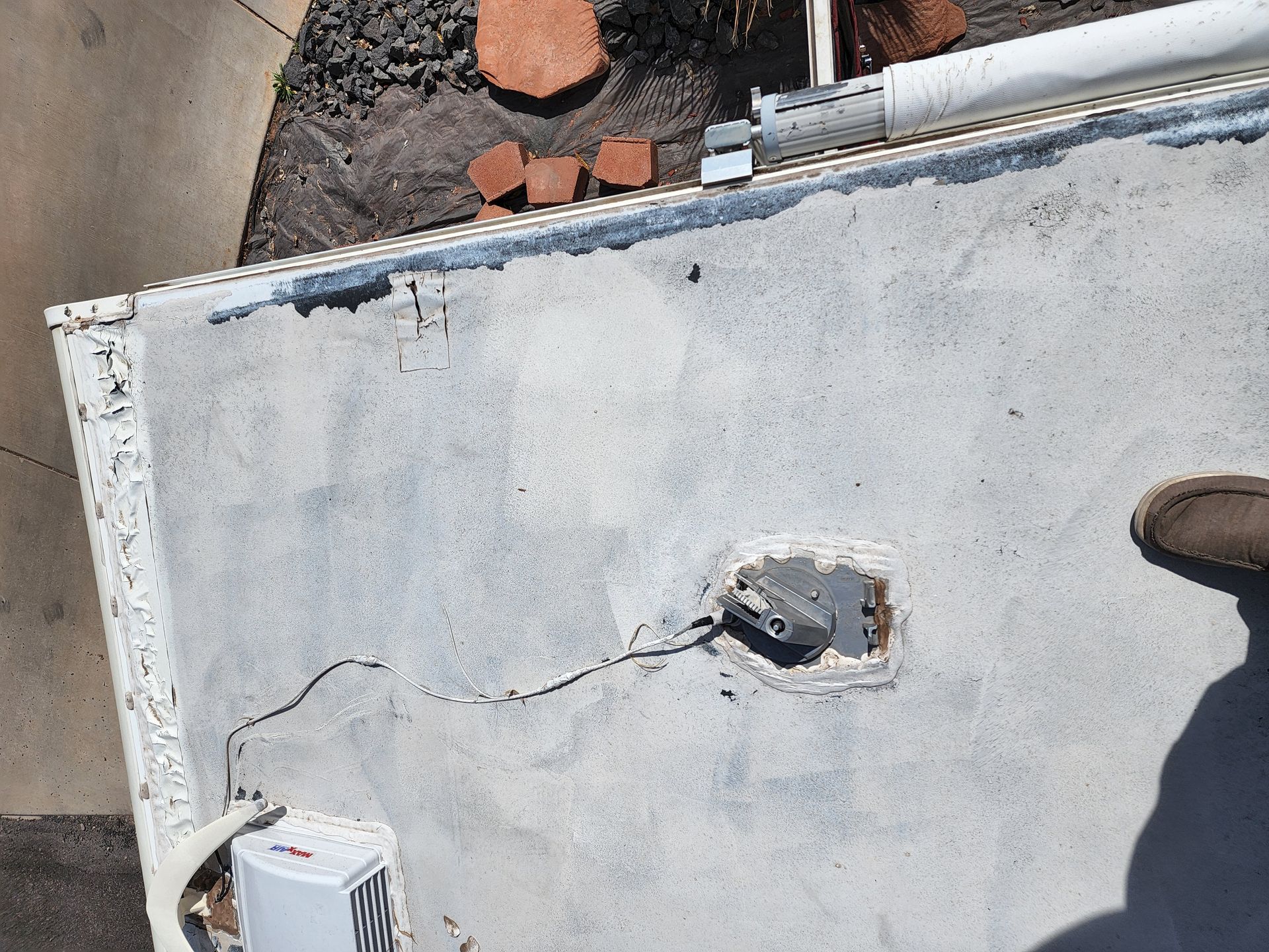 Top-down view of a cracked, light-colored roof with a circular opening and a pipe.