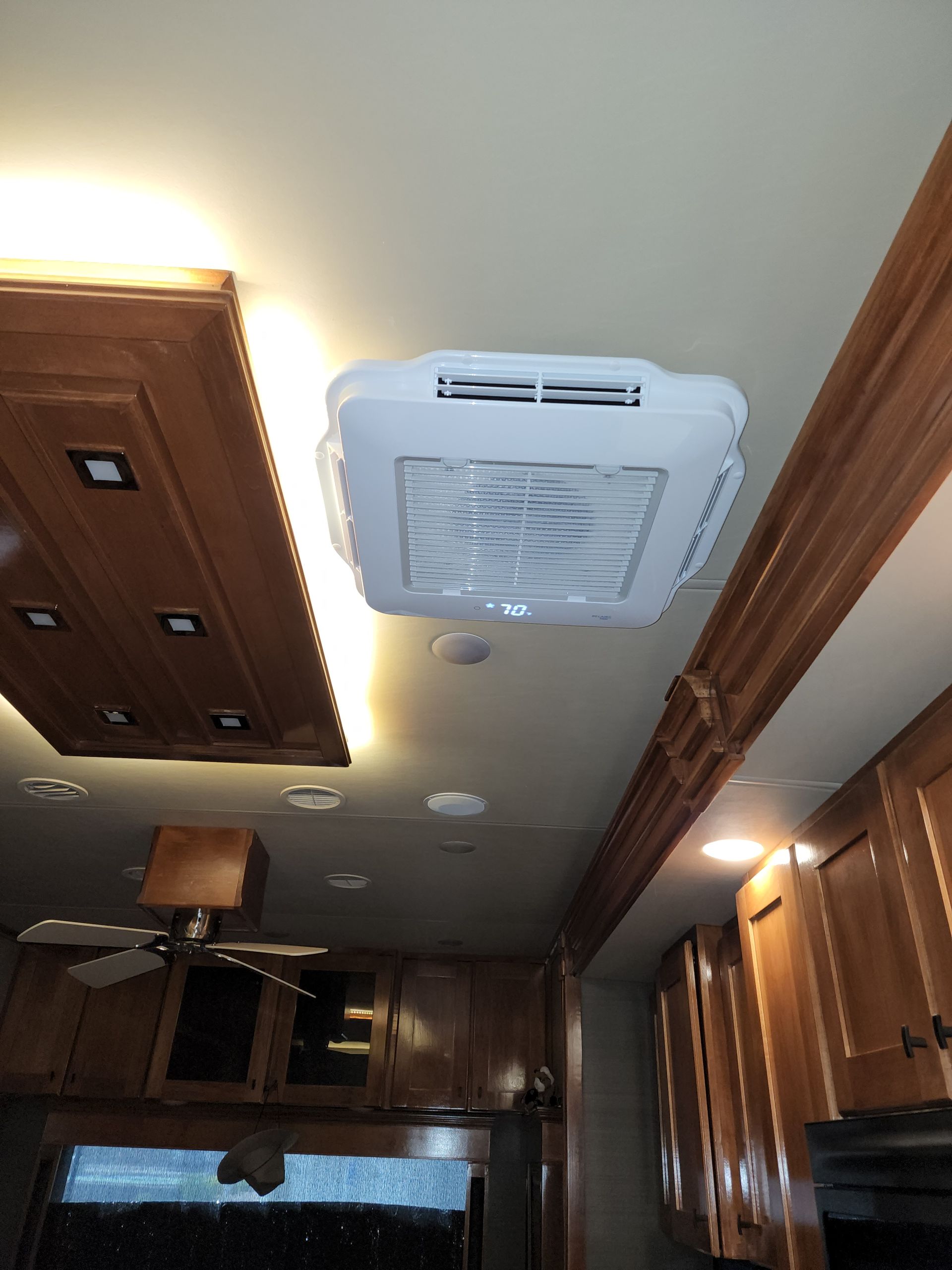 RV ceiling with air conditioner unit, brown cabinets, and overhead lighting.