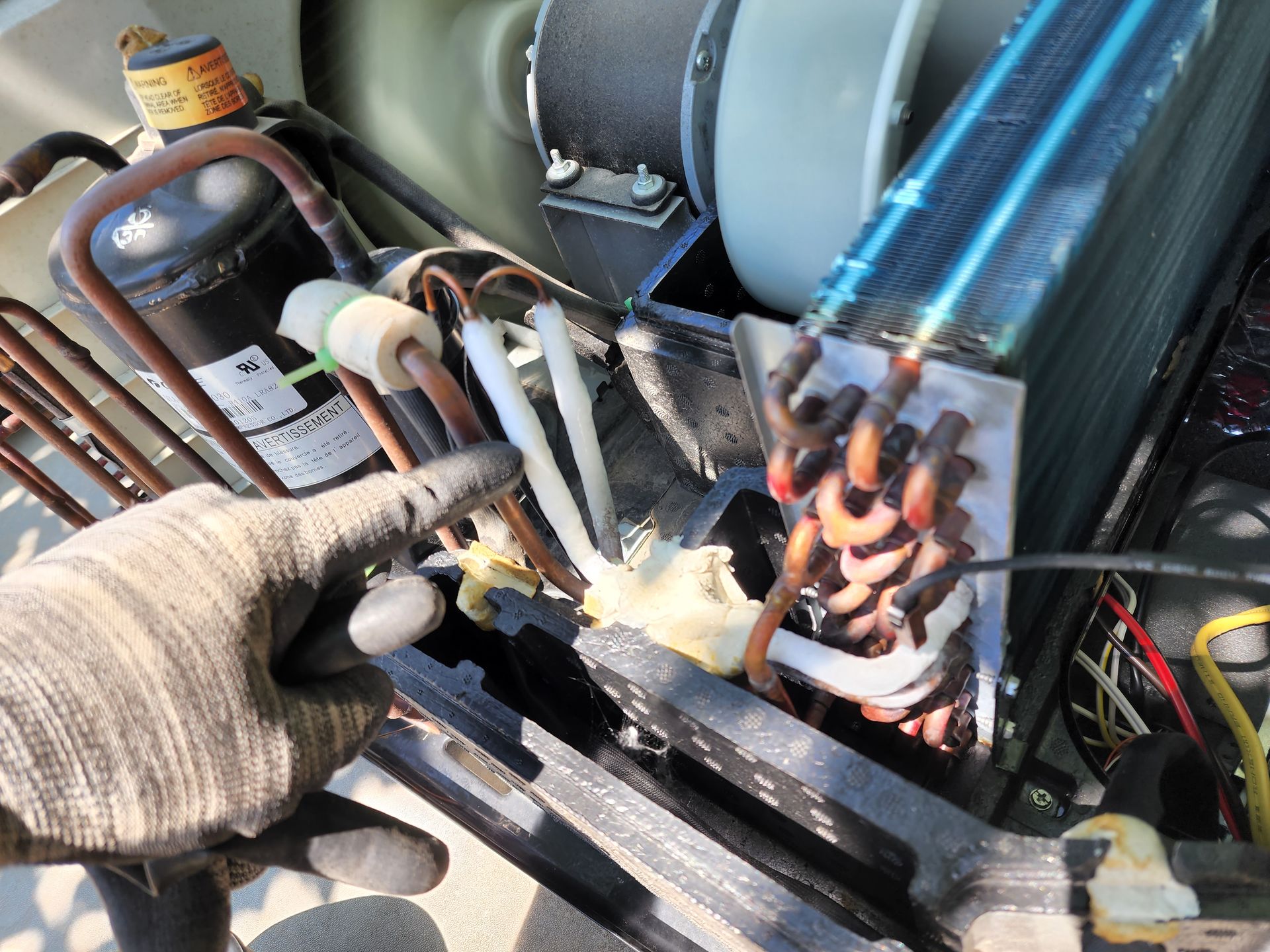 Gloved hand points to copper tubing and foam insulation inside an air conditioning unit.
