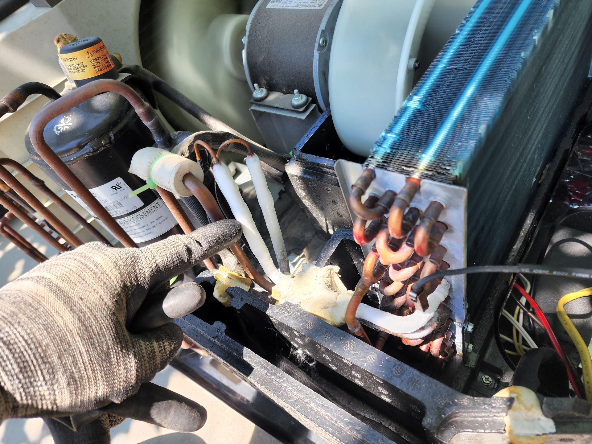 Person using pliers on copper tubing of an air conditioning unit.