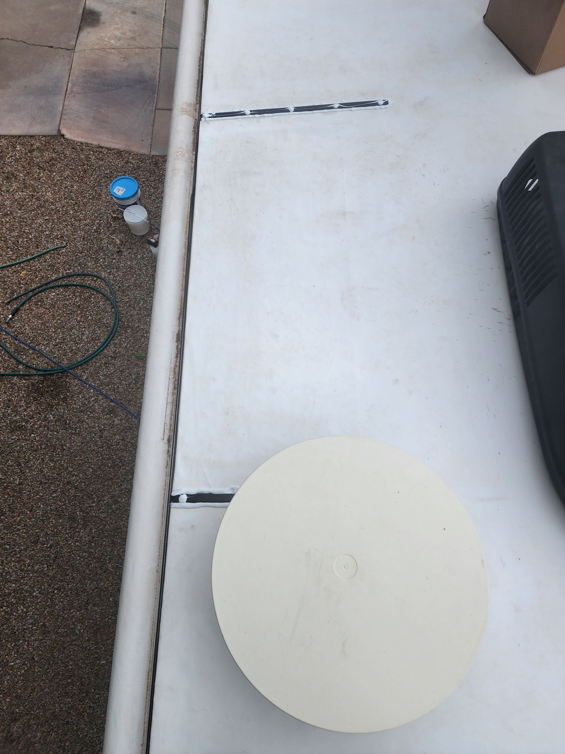 White pool cover partially unrolled, gravel and pavers visible.