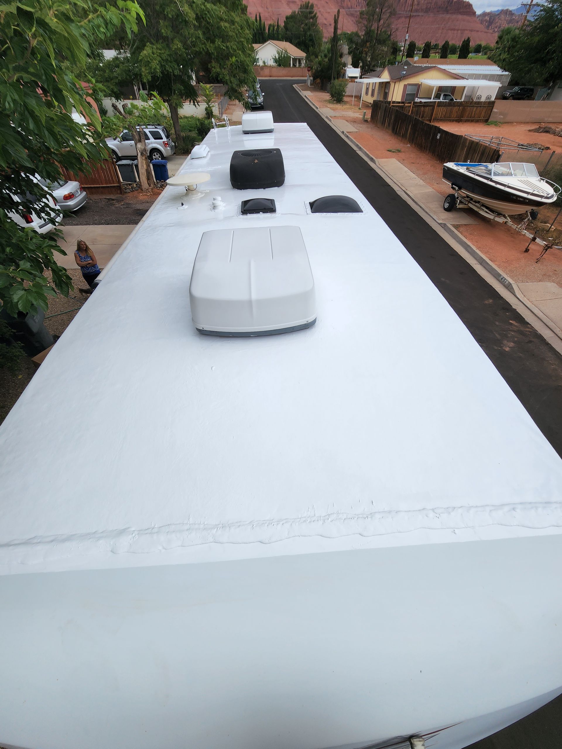 Overhead view of a white RV roof with air conditioning units and a boat on a trailer parked nearby.
