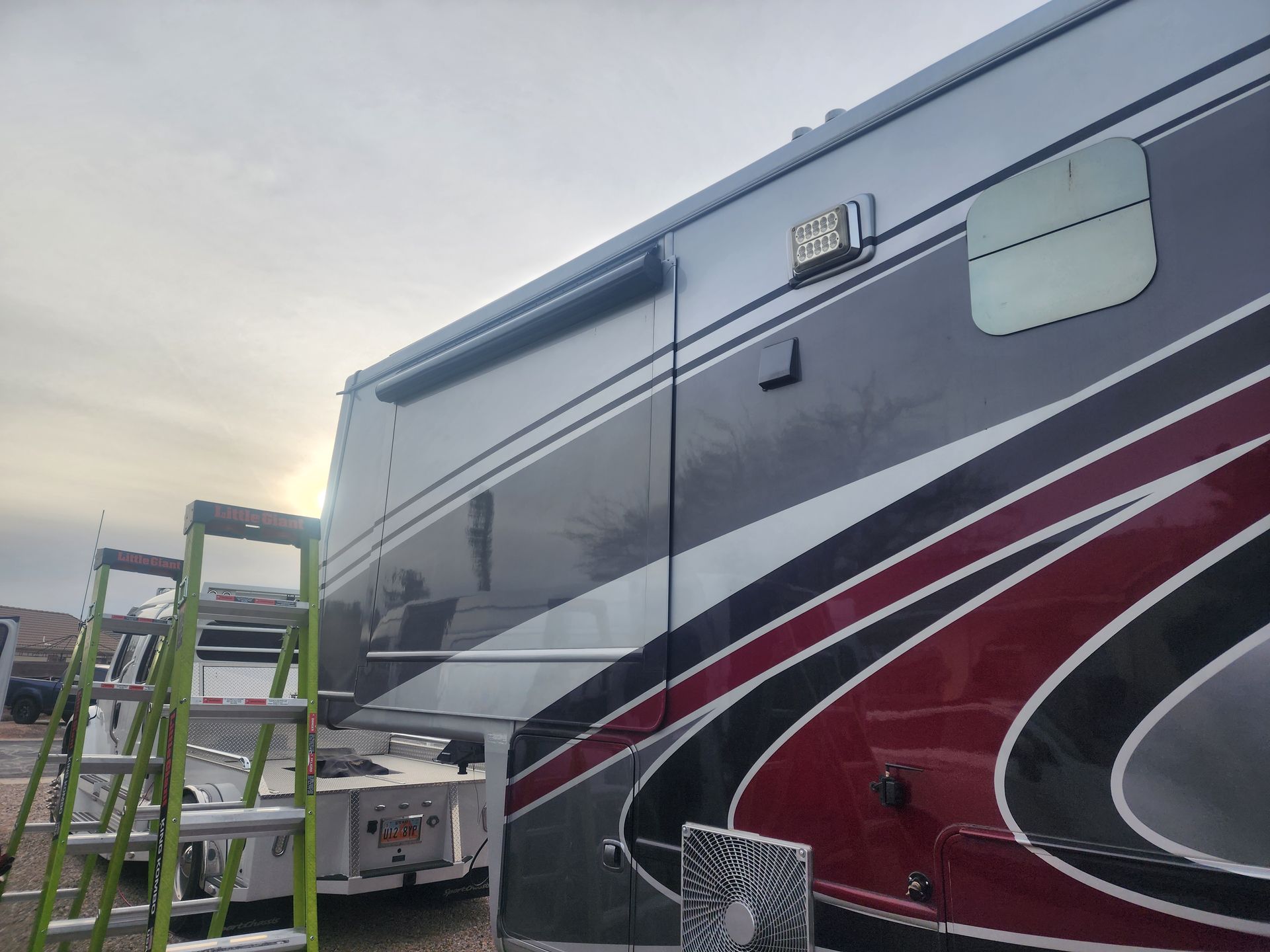 Motorhome with gray, red, and black paint, a retractable awning, and a ladder beside it.