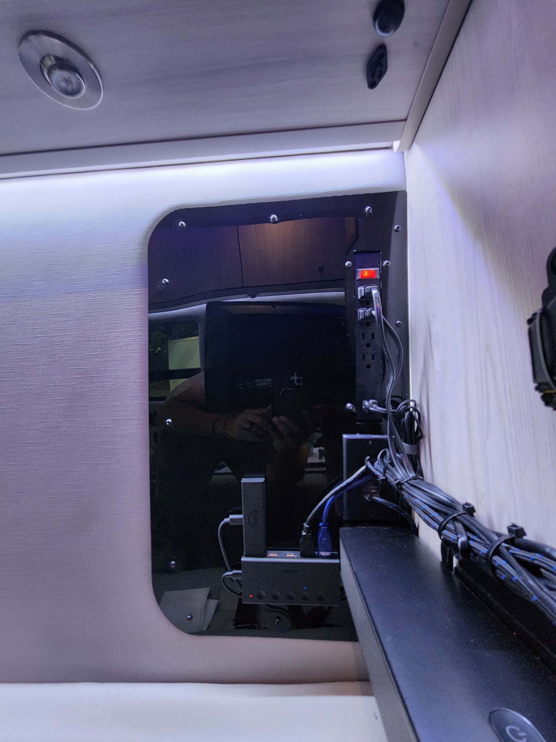 Interior of a vehicle, showing a mounted screen with various connected cables, lights and dark walls.