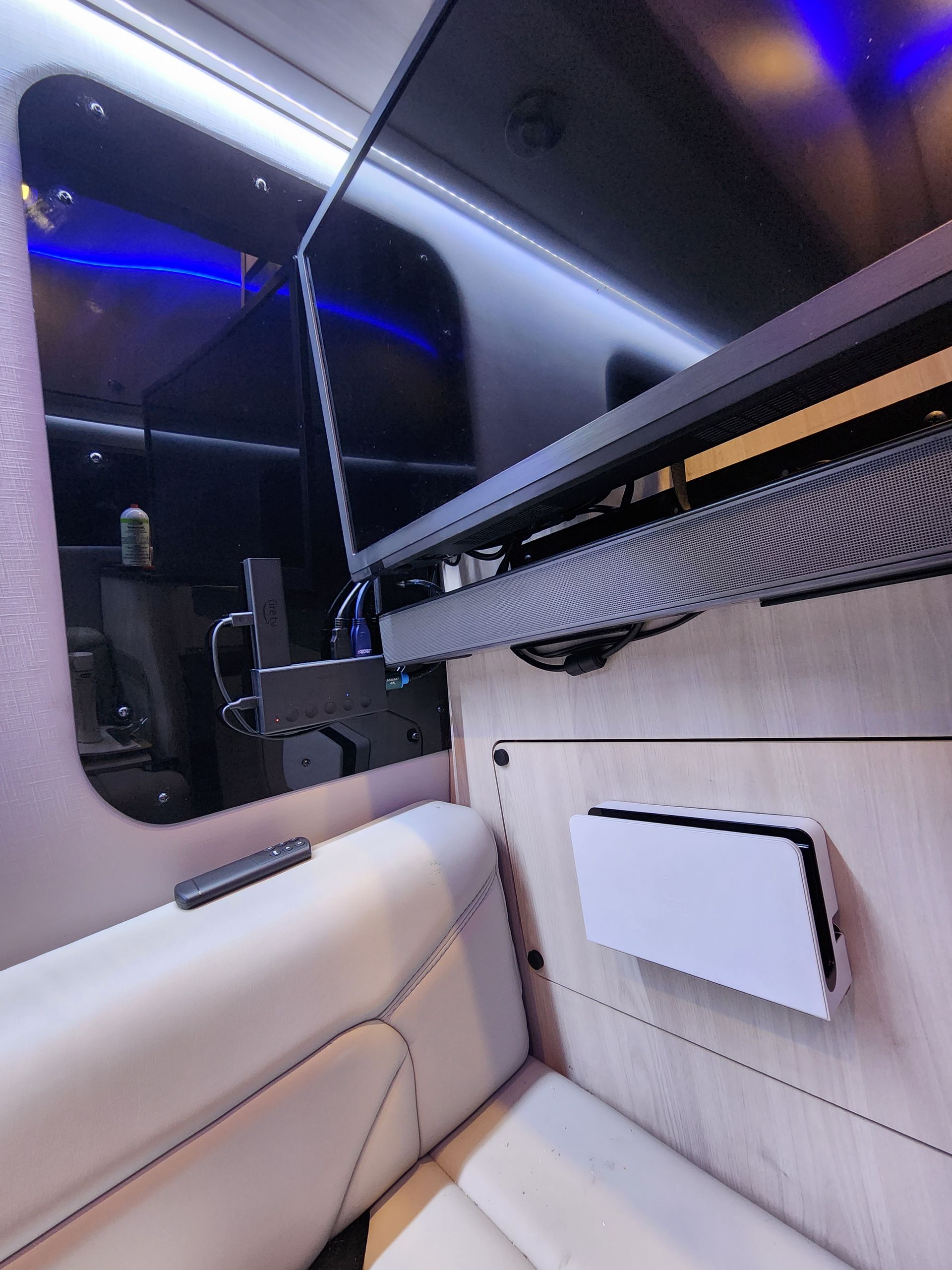 Interior of a van with a mounted TV, soundbar, and a console, near white leather seats.
