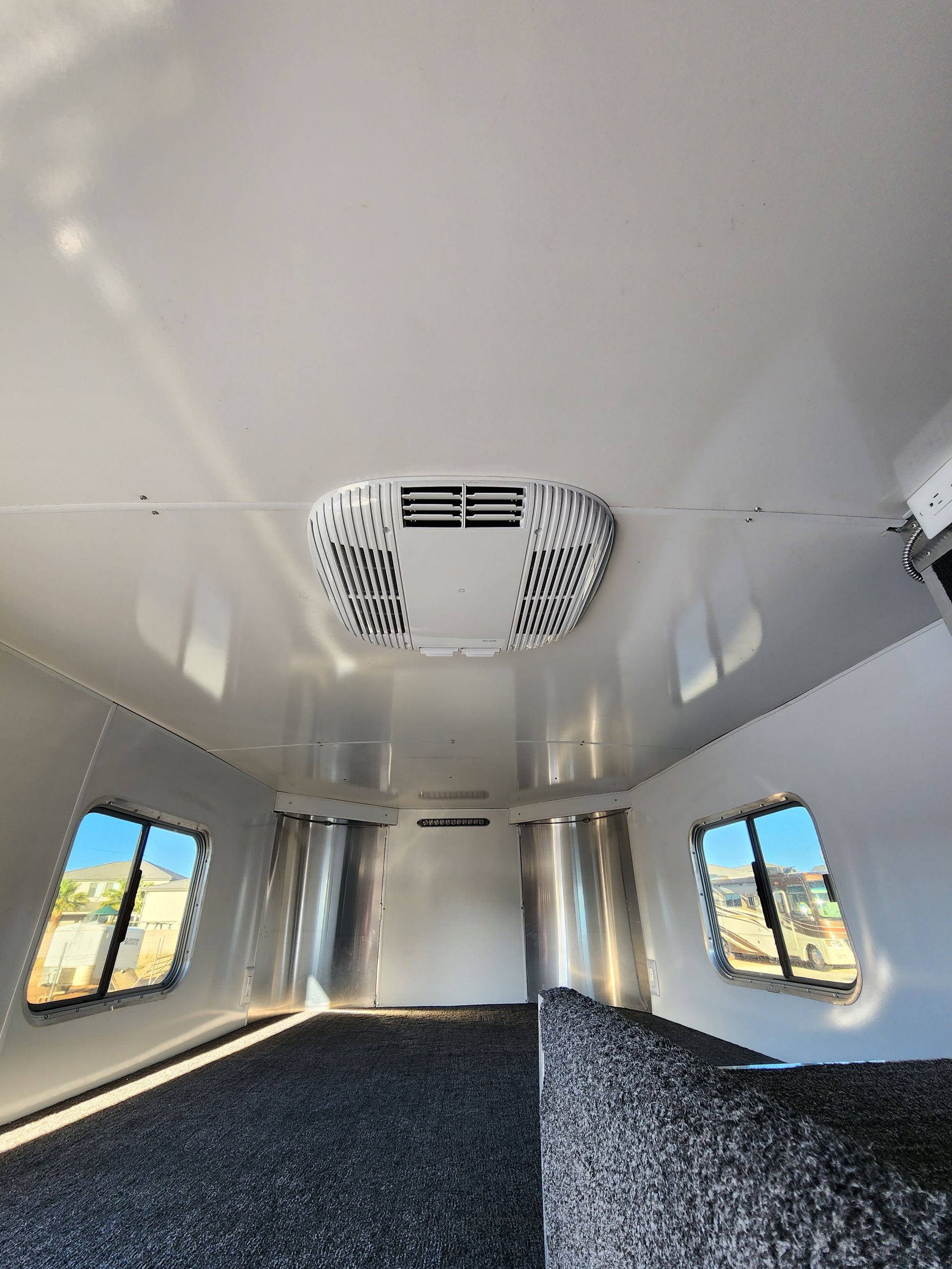 Interior of a white horse trailer with air conditioning unit on the ceiling and windows.