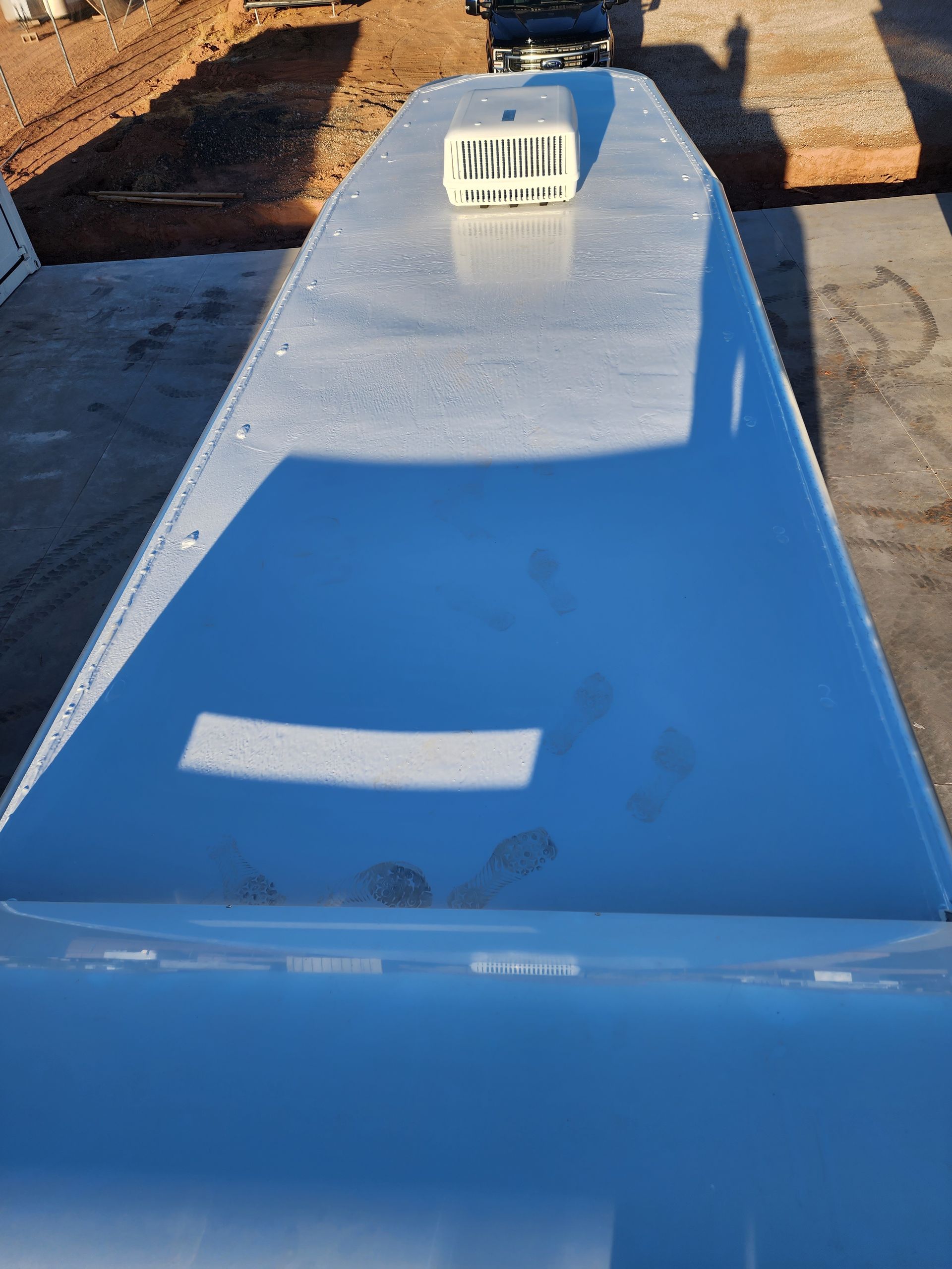 White bus roof with air vent, footprints, and shadows, viewed from above.