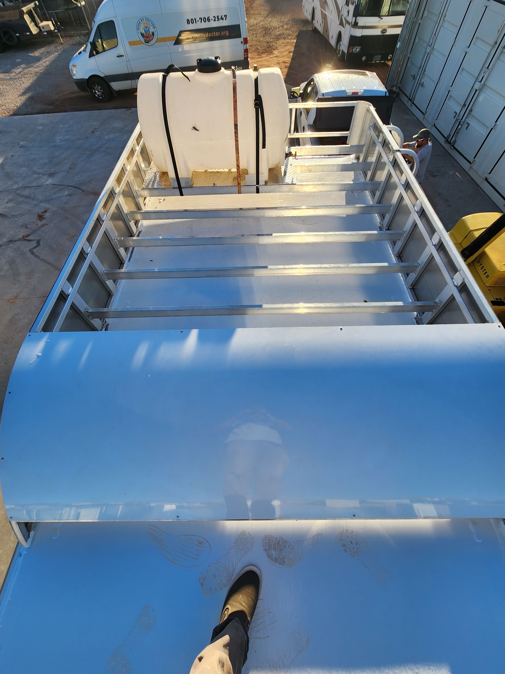 Overhead view of a vehicle bed with metal rails and steps. A white tank is secured on the bed.