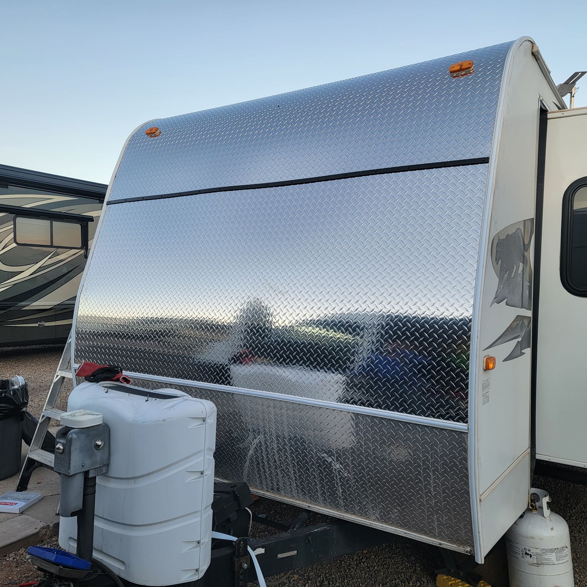 RV front covered in diamond plate metal. A propane tank and hitch are in front.