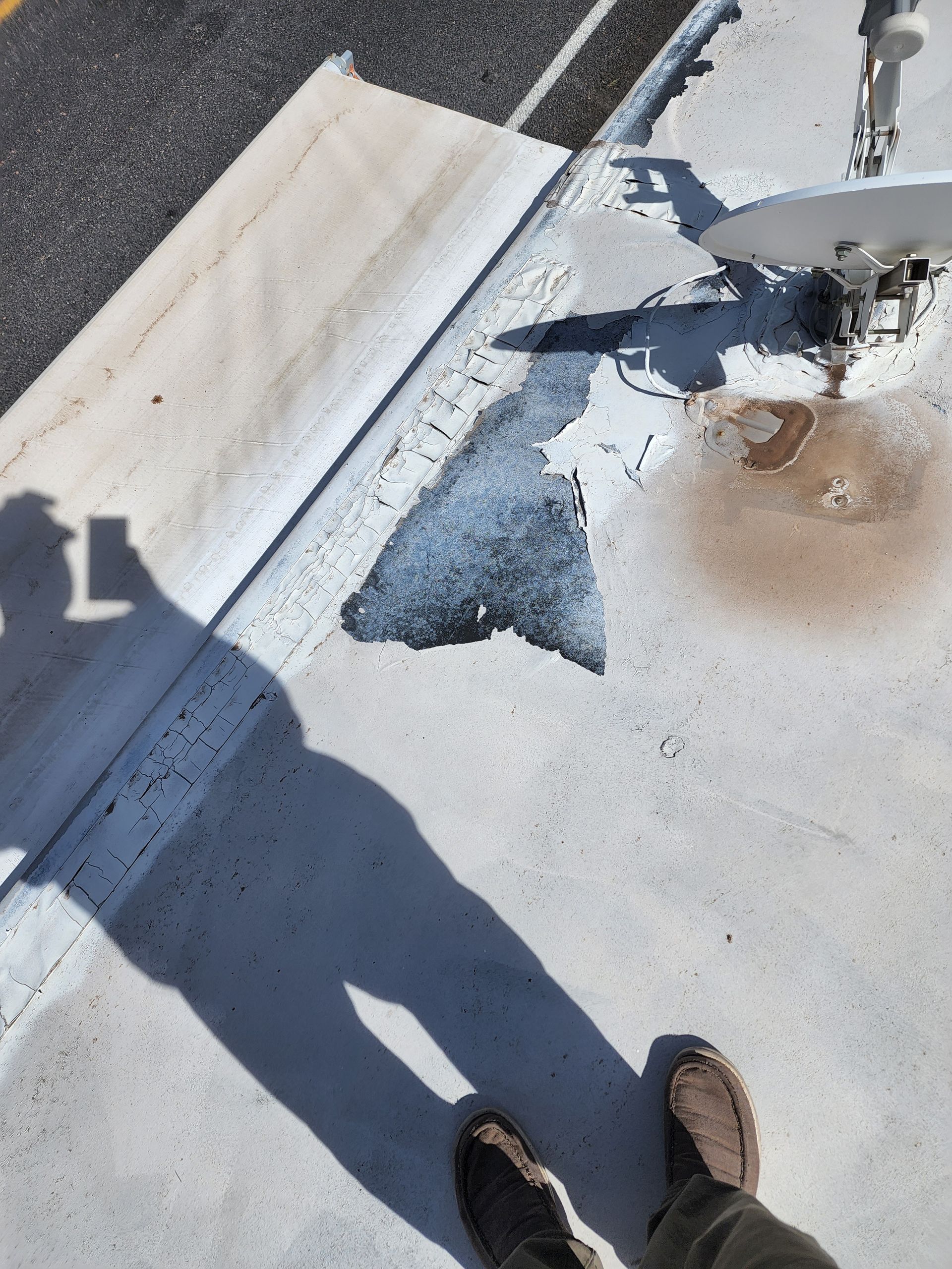 Person standing on a white surface with a shadow. There is a satellite dish and dark stains.