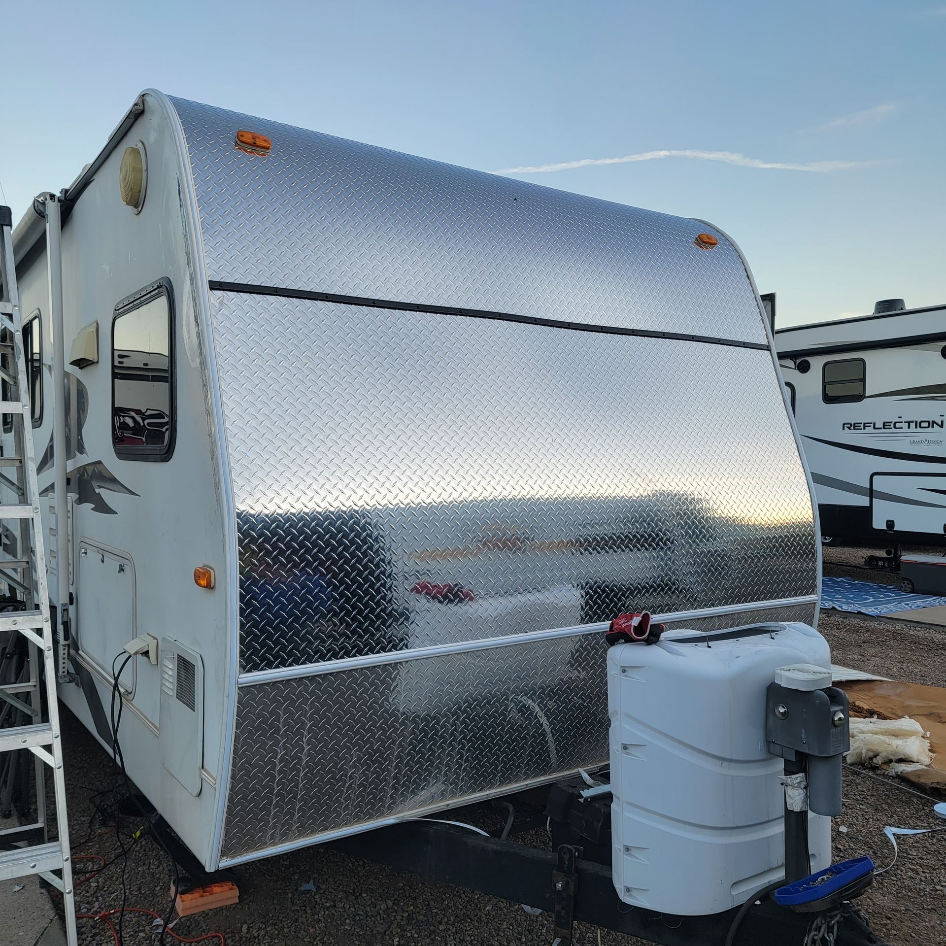 Camper trailer with aluminum diamond plate front. Blue propane tank in front.