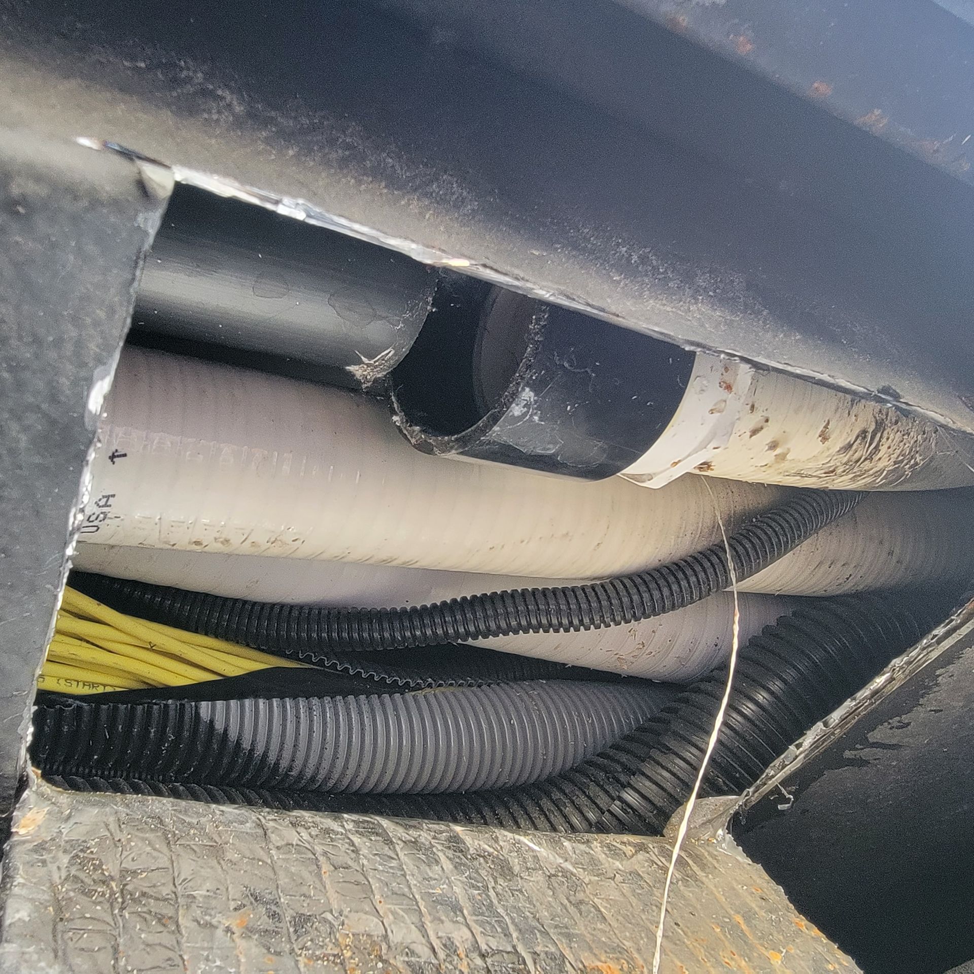 Pipes and wires visible through a rectangular opening in a dark surface. Black, white, and yellow colors are present.