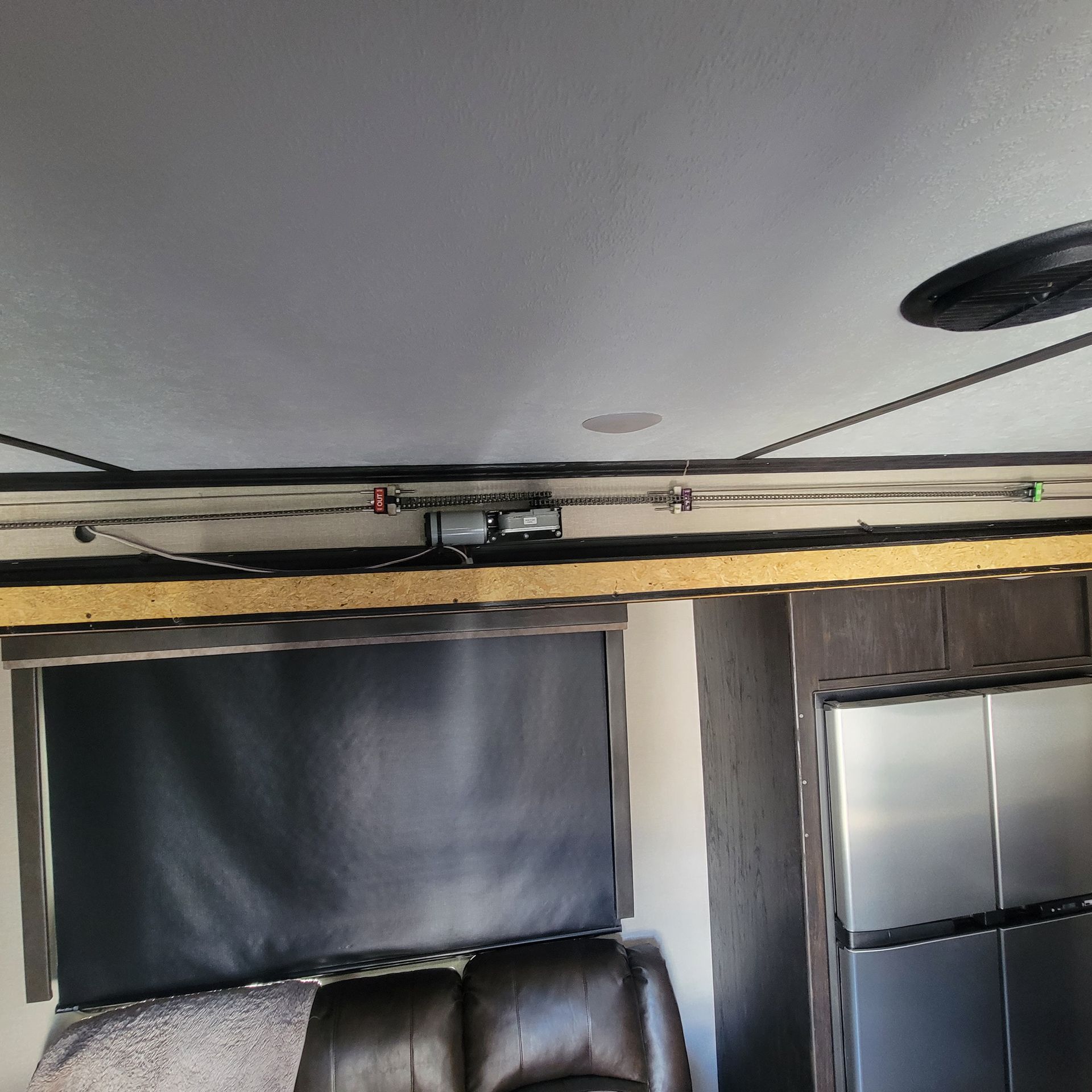 Interior of an RV with a dark window shade, brown recliner, and metal refrigerator.