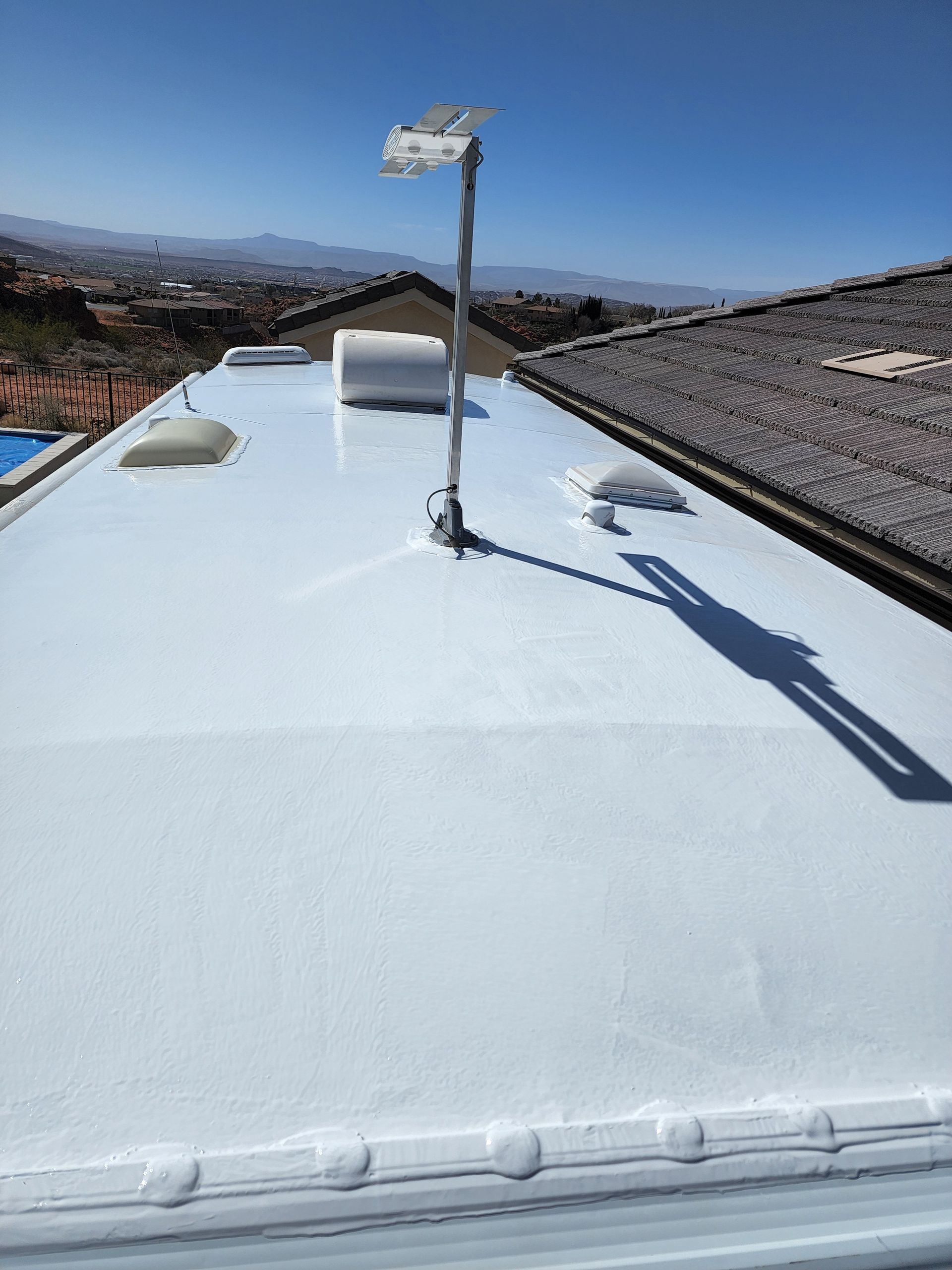 White RV roof with a radio antenna, skylights, and vent pipes, on a sunny day.
