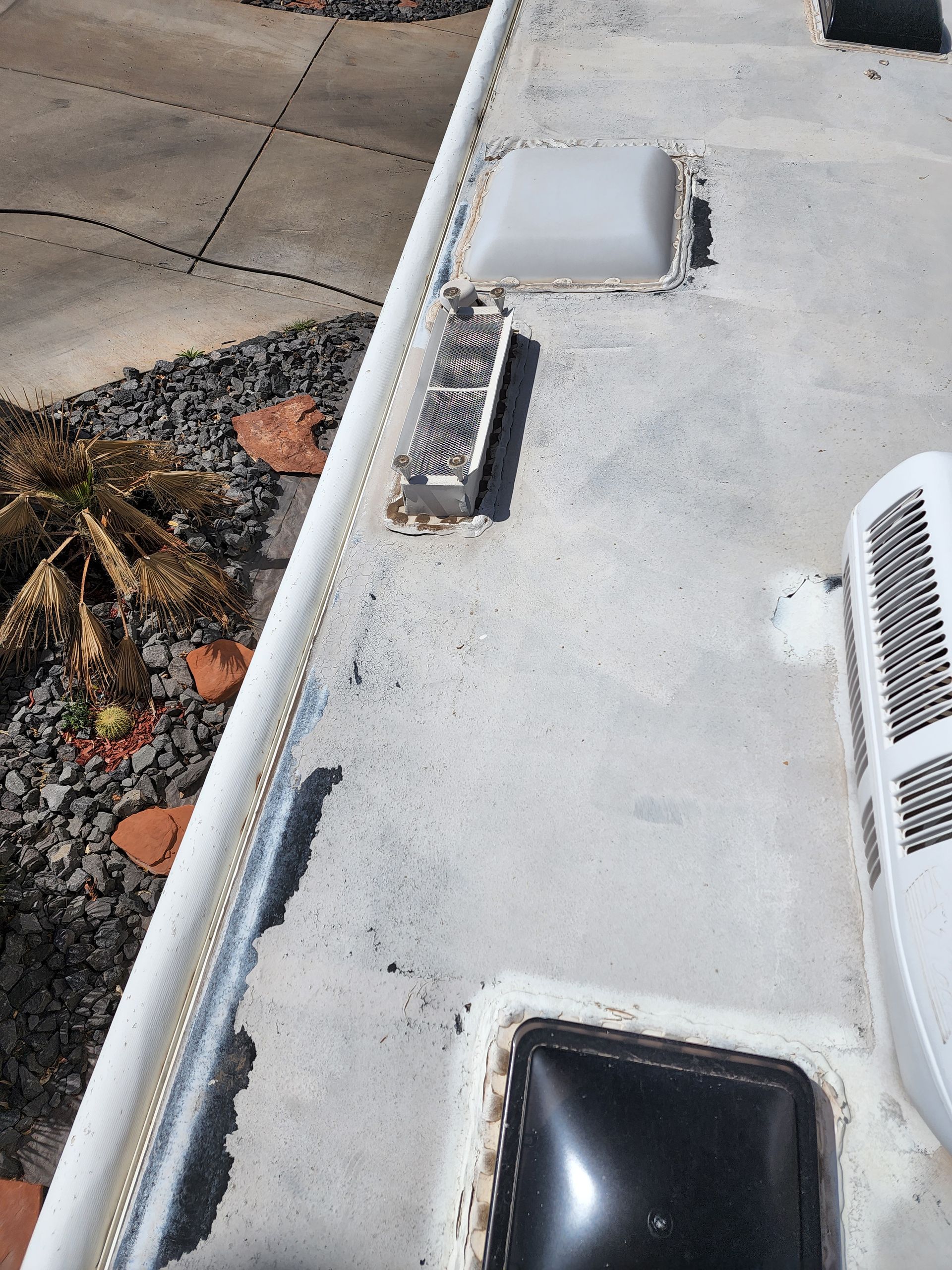 RV roof with vents, air conditioner, and weathered sealant, showing potential leaks and damage.