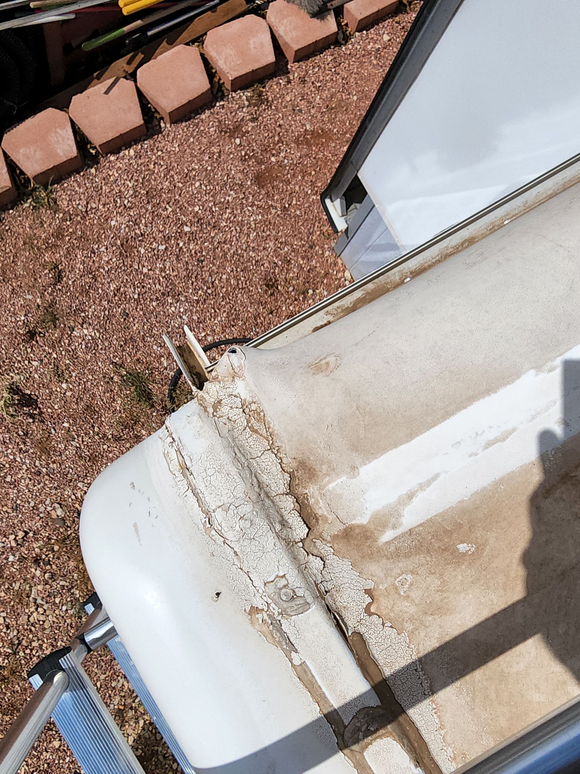 Overhead view of a white RV roof showing cracked sealant and discoloration near the edge.