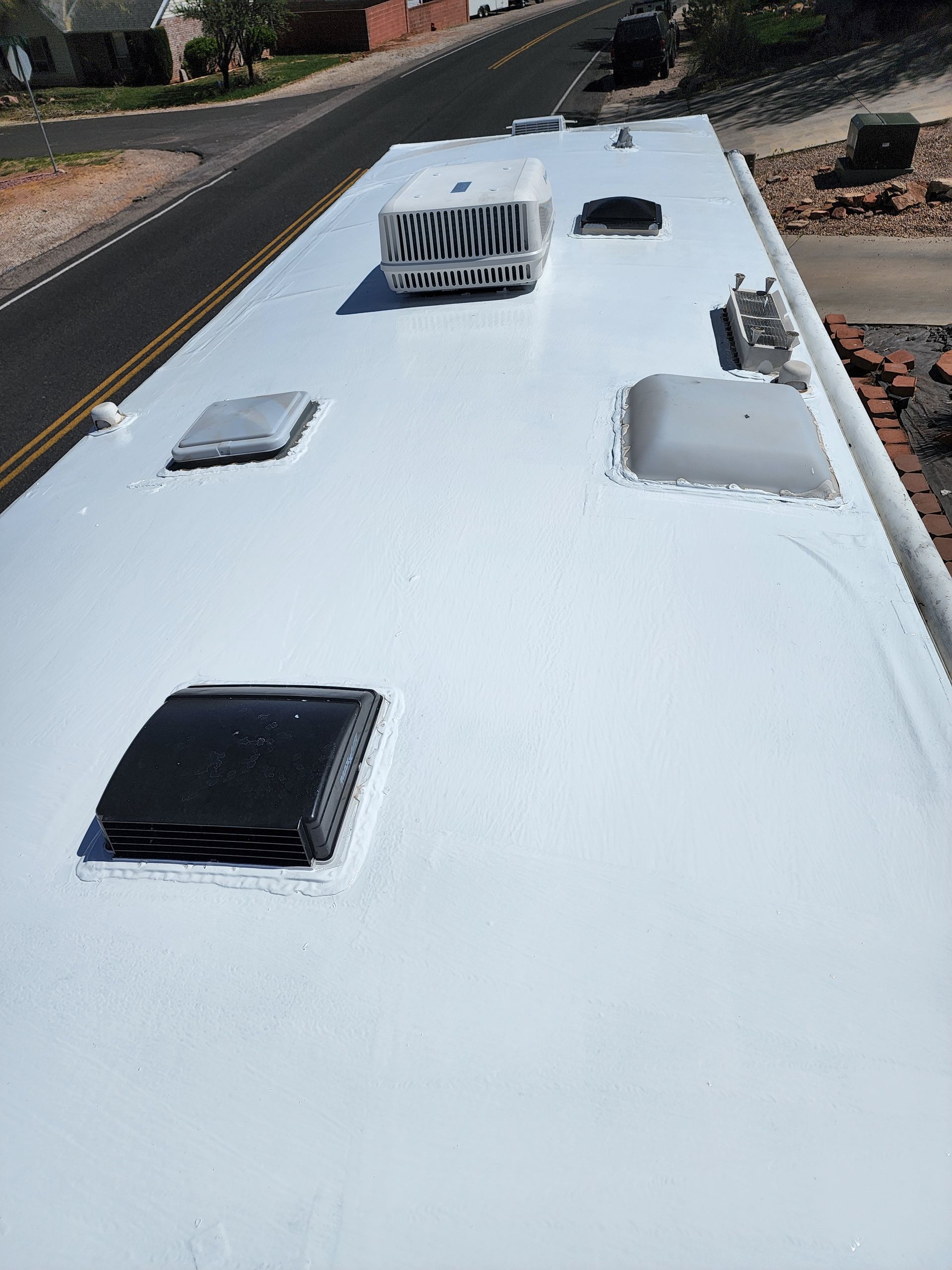 White RV roof with vents and air conditioning unit, viewed from above, with street in the background.