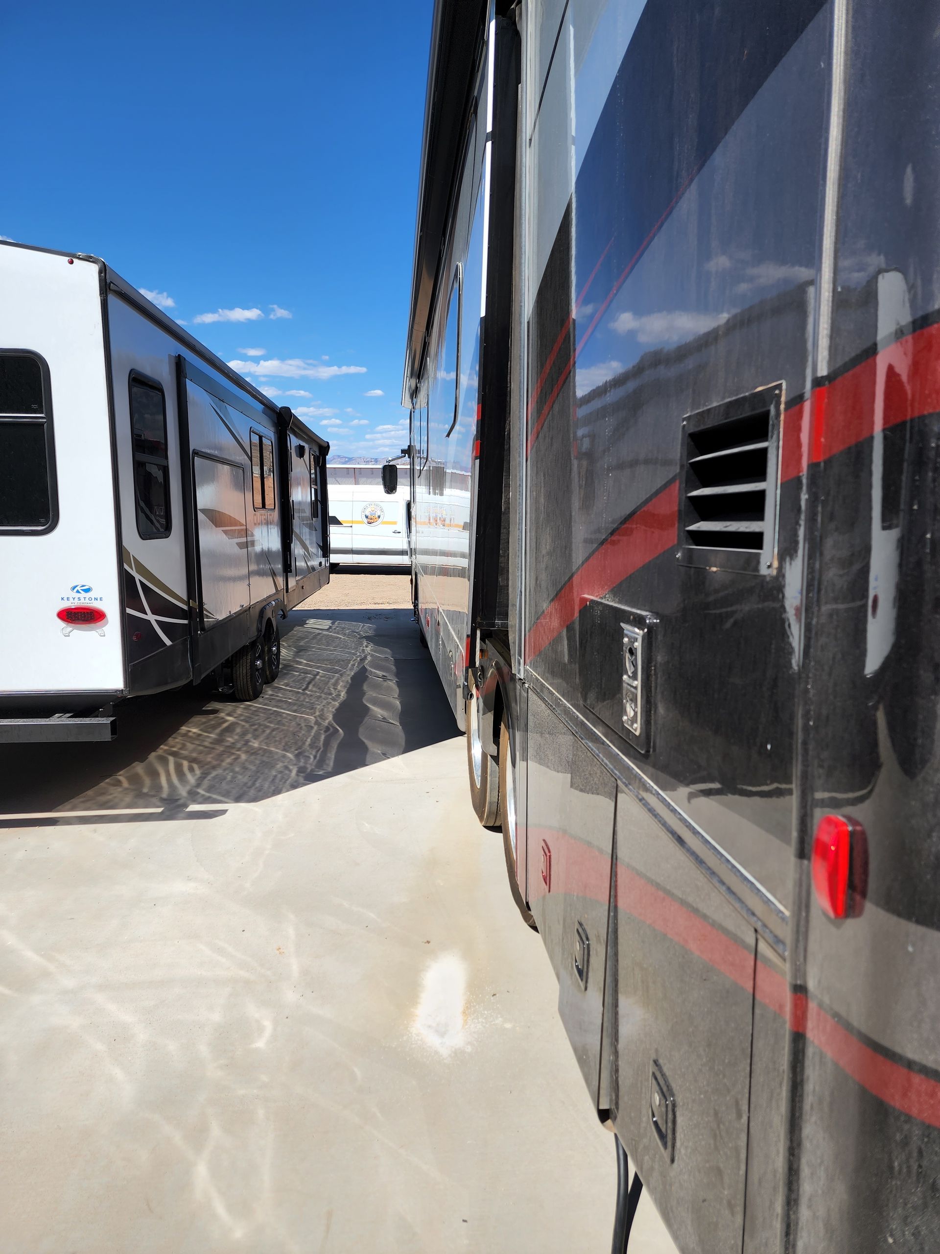 RV parked next to a trailer under a bright blue sky. Black and red detailing on RV.