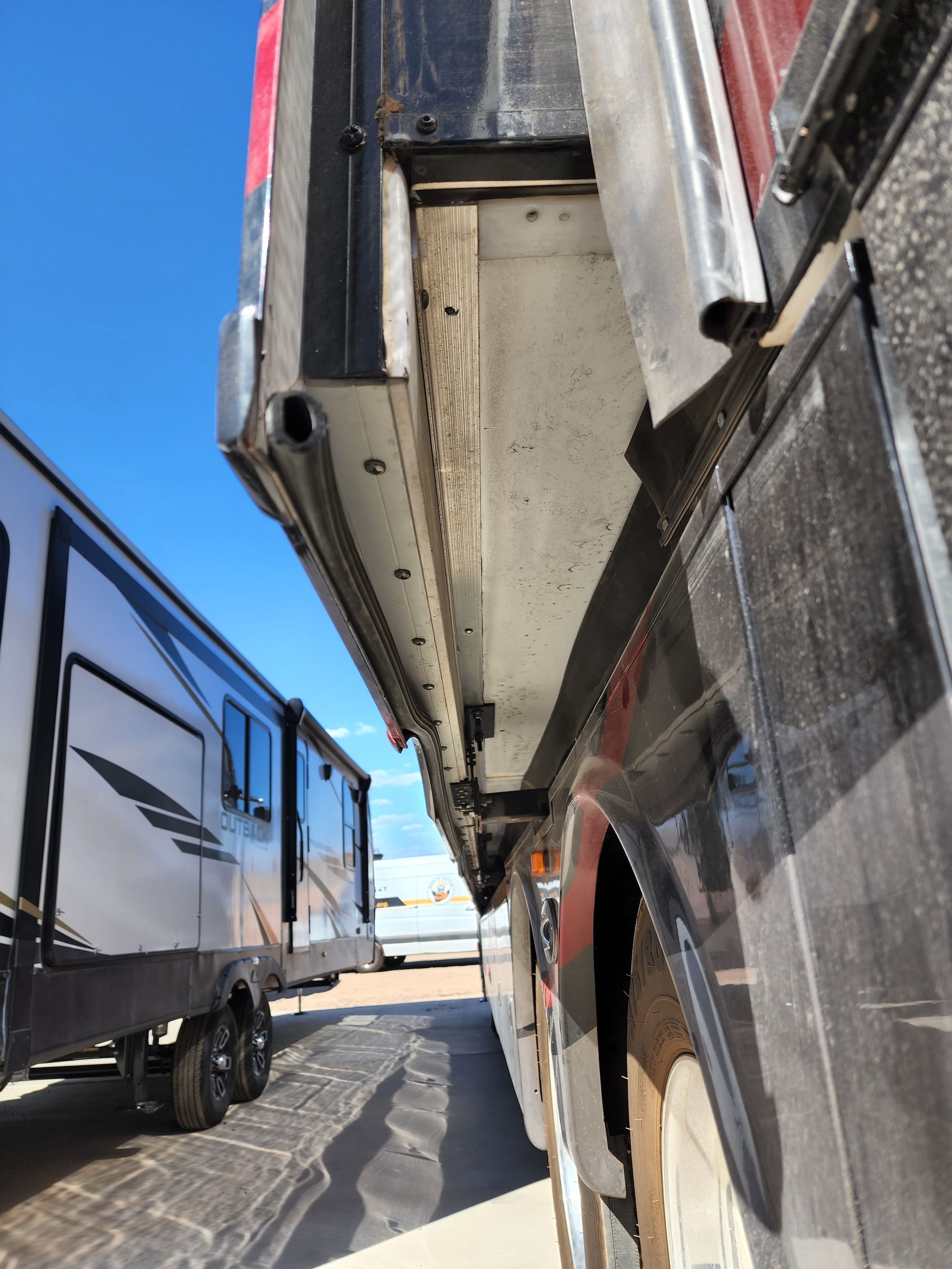 RV side with open compartment next to a trailer under a blue sky.
